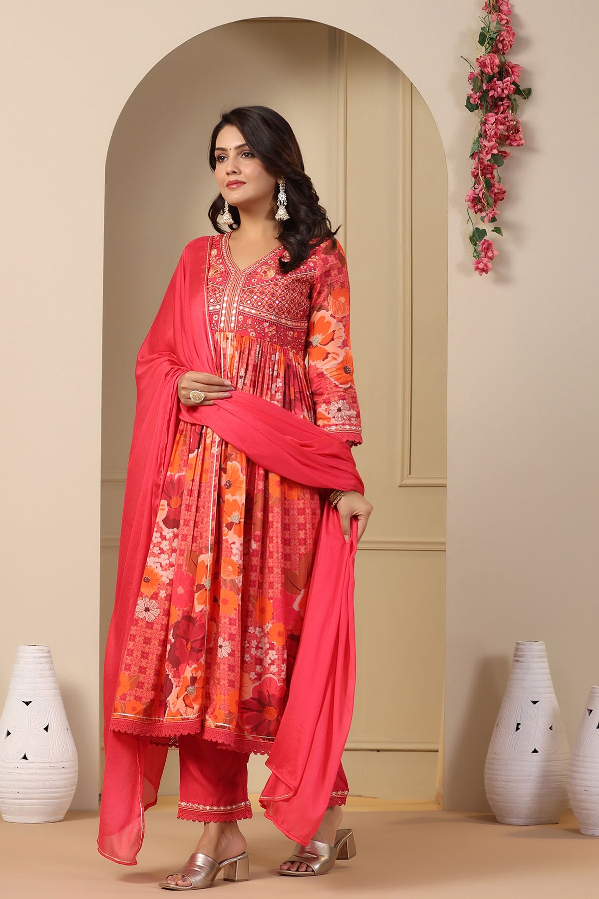 Woman in a pink and orange traditional outfit standing in a decorated room.