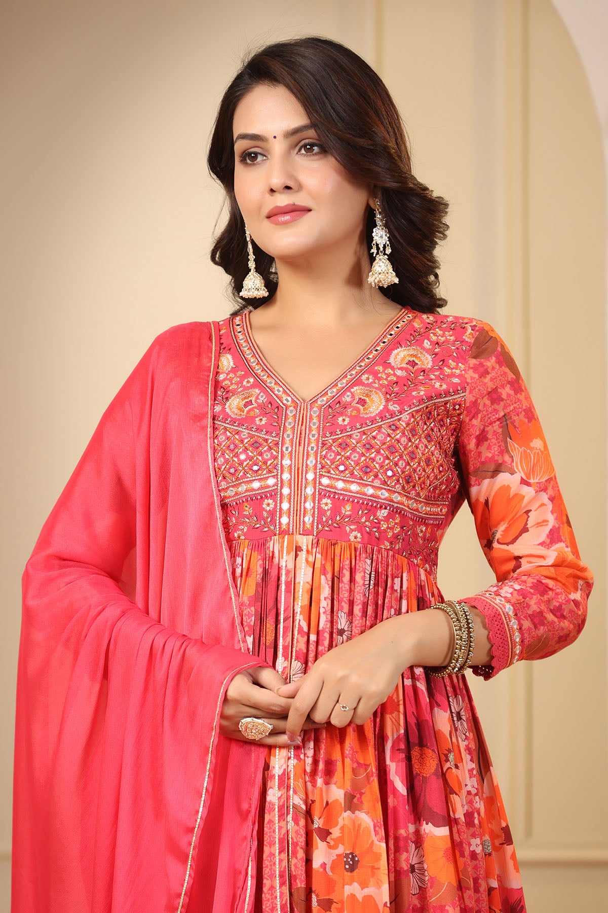 Woman wearing a colorful traditional outfit with a pink dupatta against a beige background