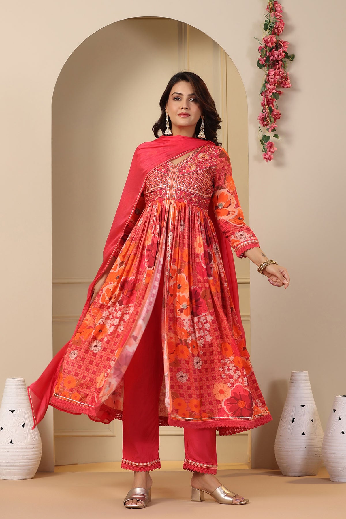 Woman wearing a traditional outfit with a red and orange patterned dress in a decorated room.