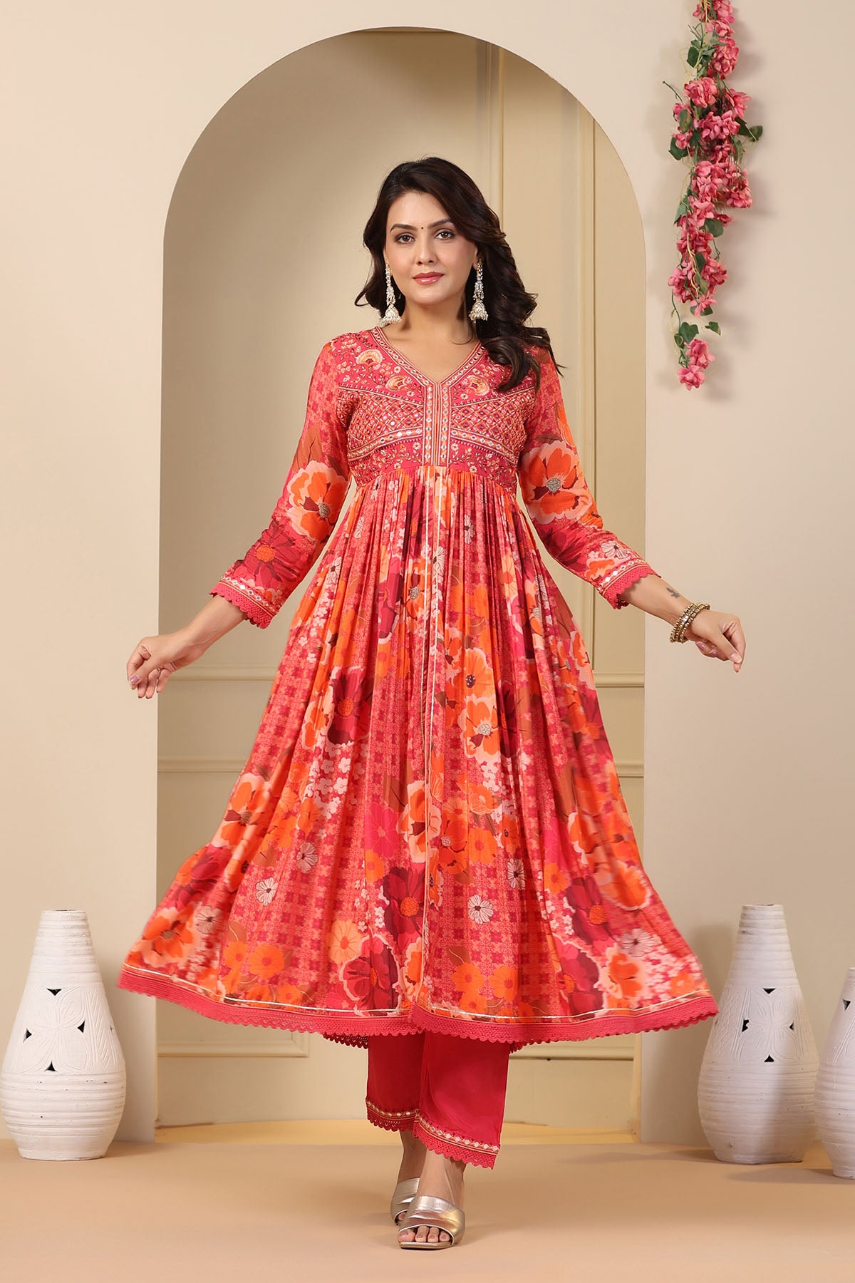 Woman wearing a red and orange floral dress standing in front of a decorative archway.
