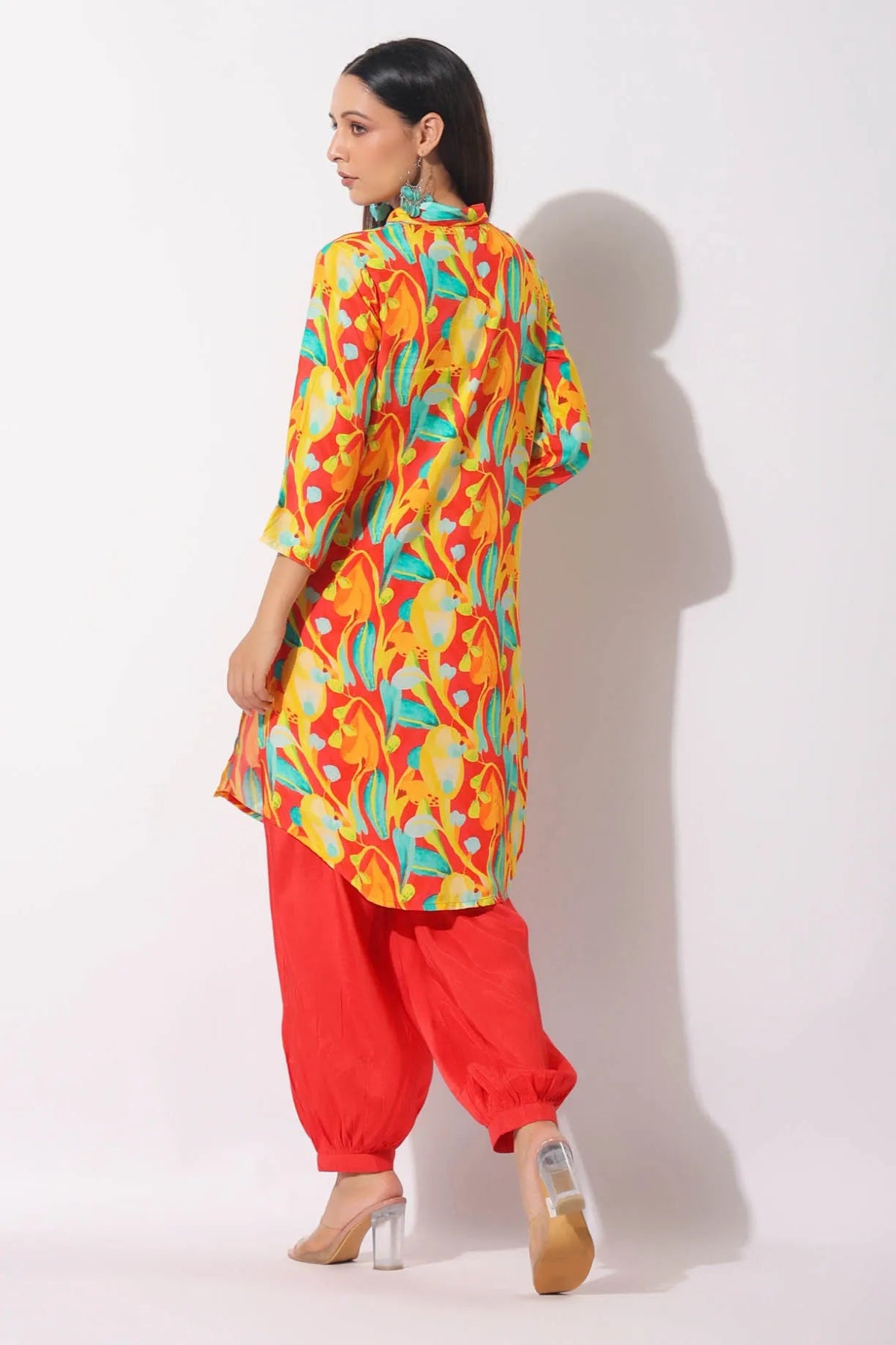 Woman wearing a colorful patterned kurta with red pants on a white background