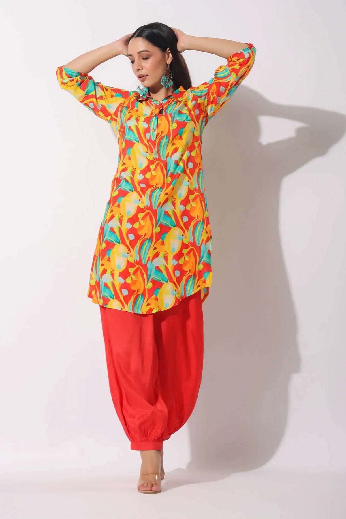 Woman wearing a colorful patterned top and red pants on a white background
