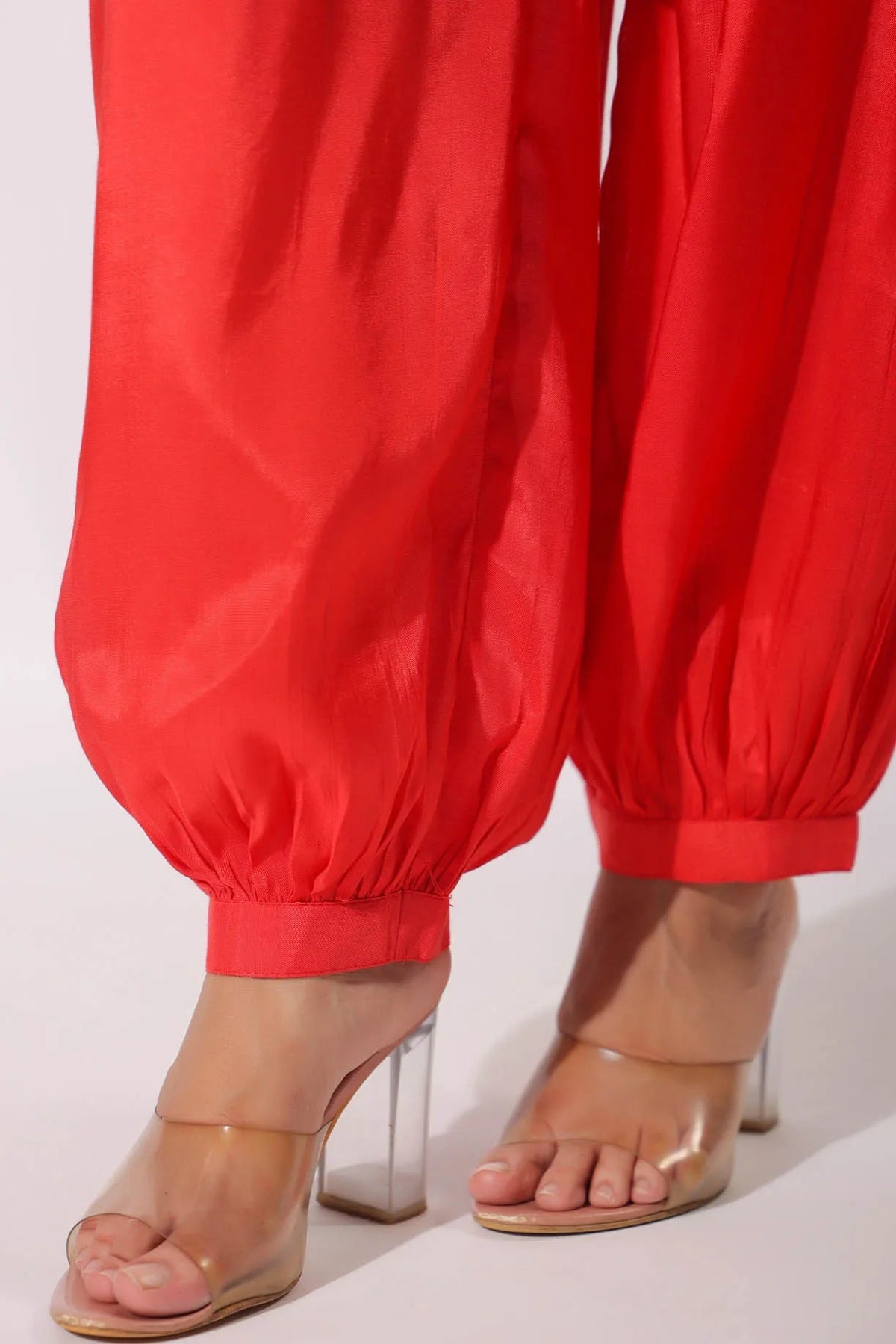 Red pants worn with clear high-heeled sandals on a white background