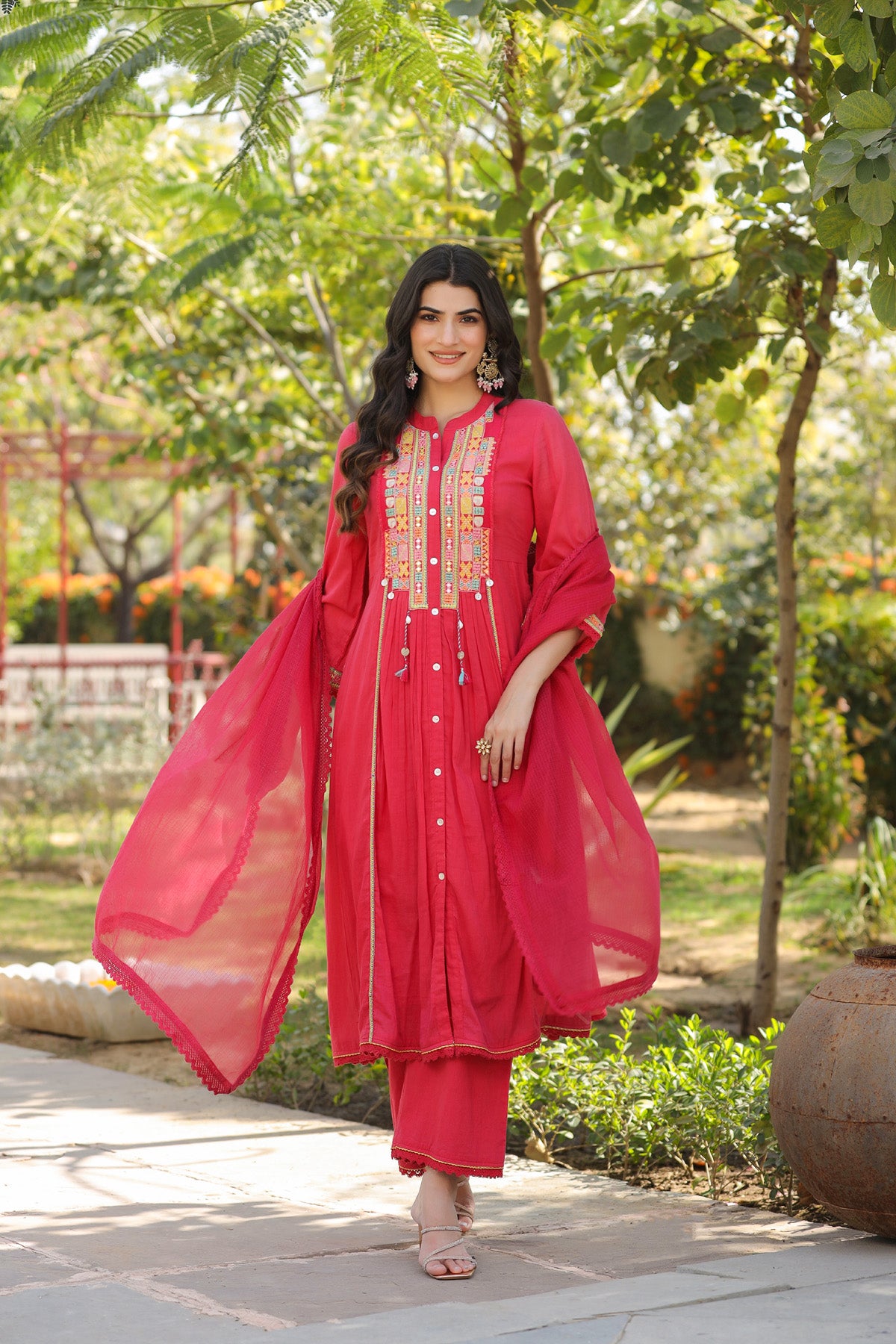 Woman in a red traditional outfit standing outdoors with greenery in the background