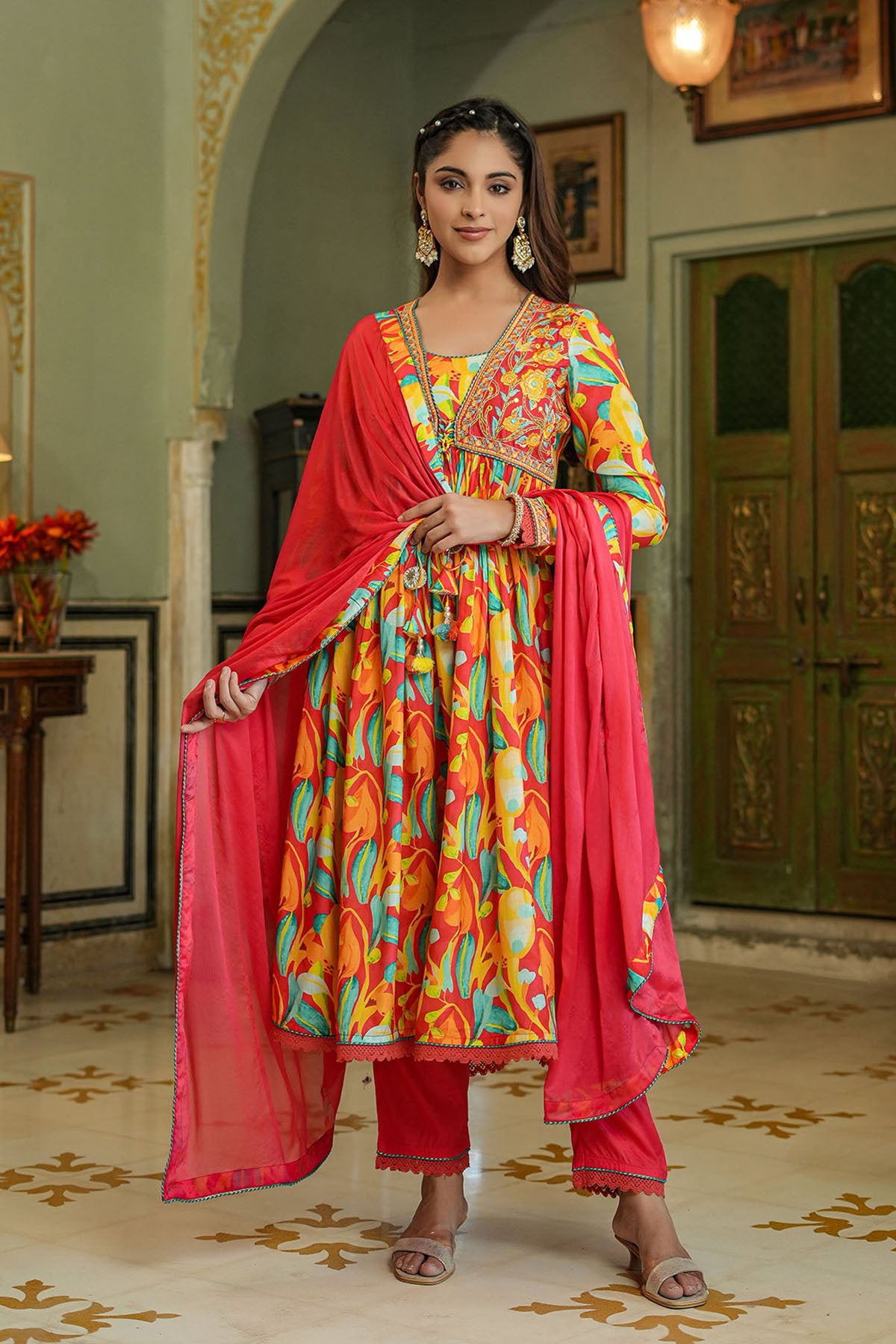 Woman in a colorful traditional outfit standing in an ornate room.