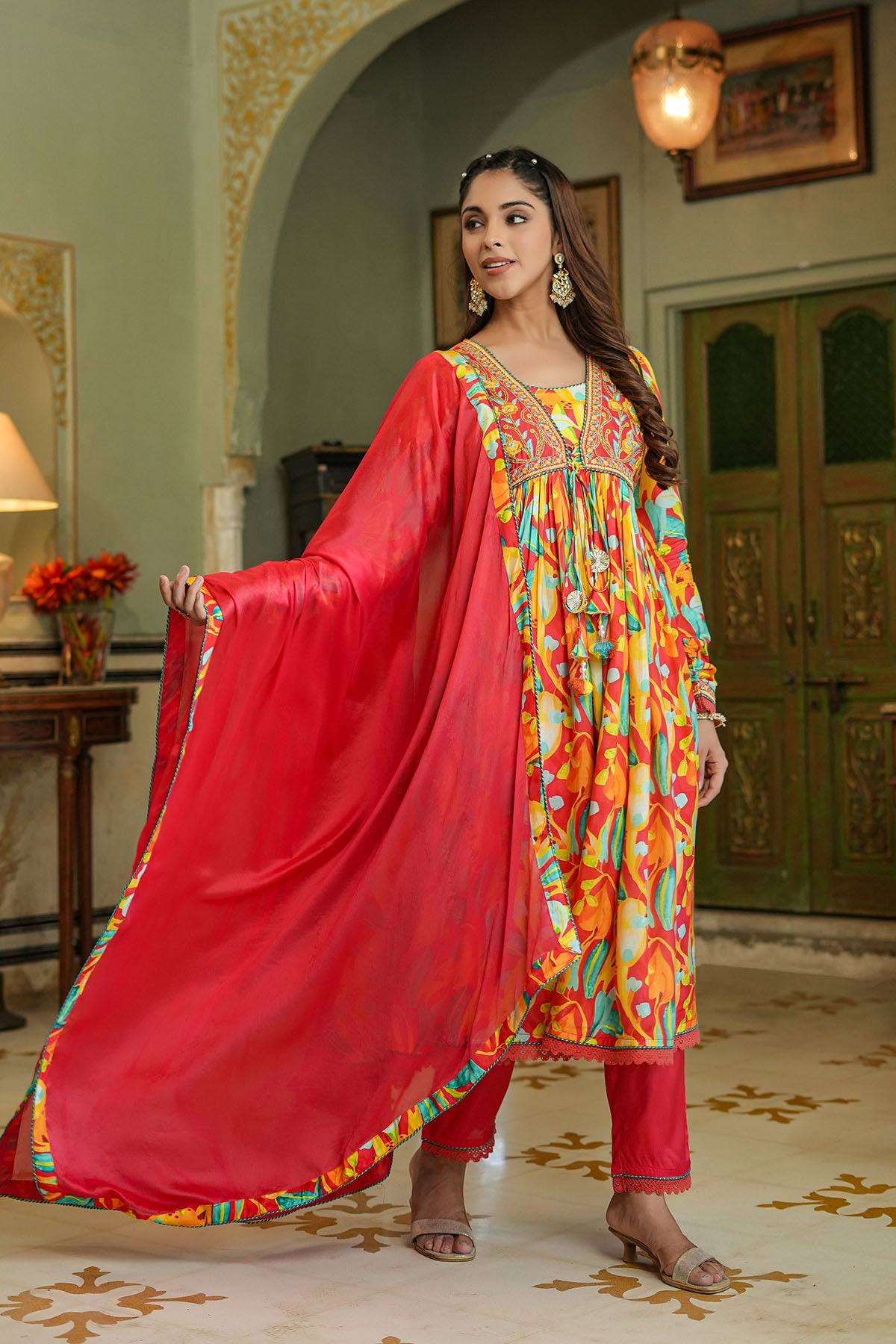 Woman in a colorful traditional outfit with a red dupatta in an ornate room.