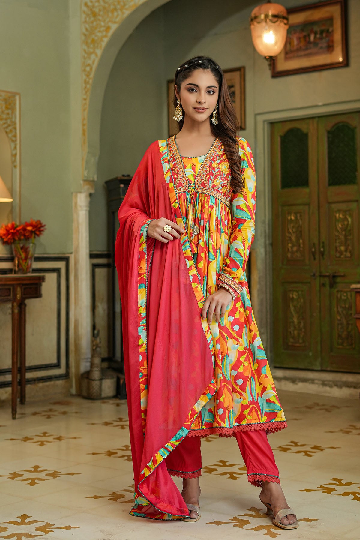 Woman in a colorful traditional outfit standing in an ornate room.