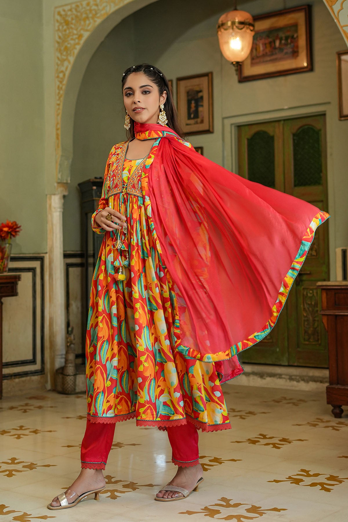 Woman in colorful traditional outfit with a red dupatta in an indoor setting