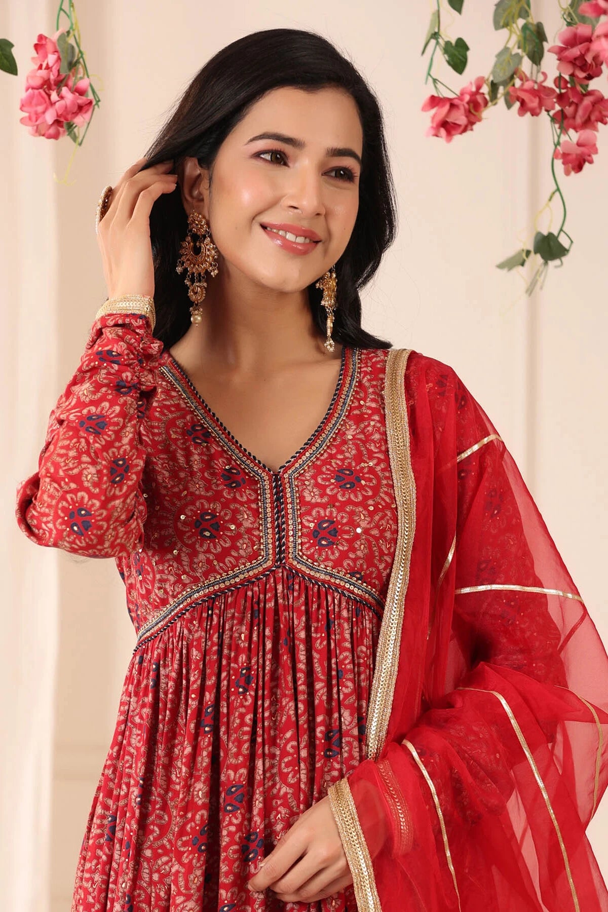 Woman wearing a red traditional outfit with floral patterns against a floral background
