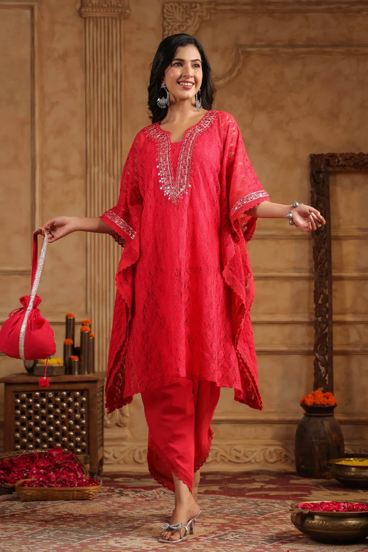Woman in a red traditional outfit standing in a decorated room with flowers and decor items.