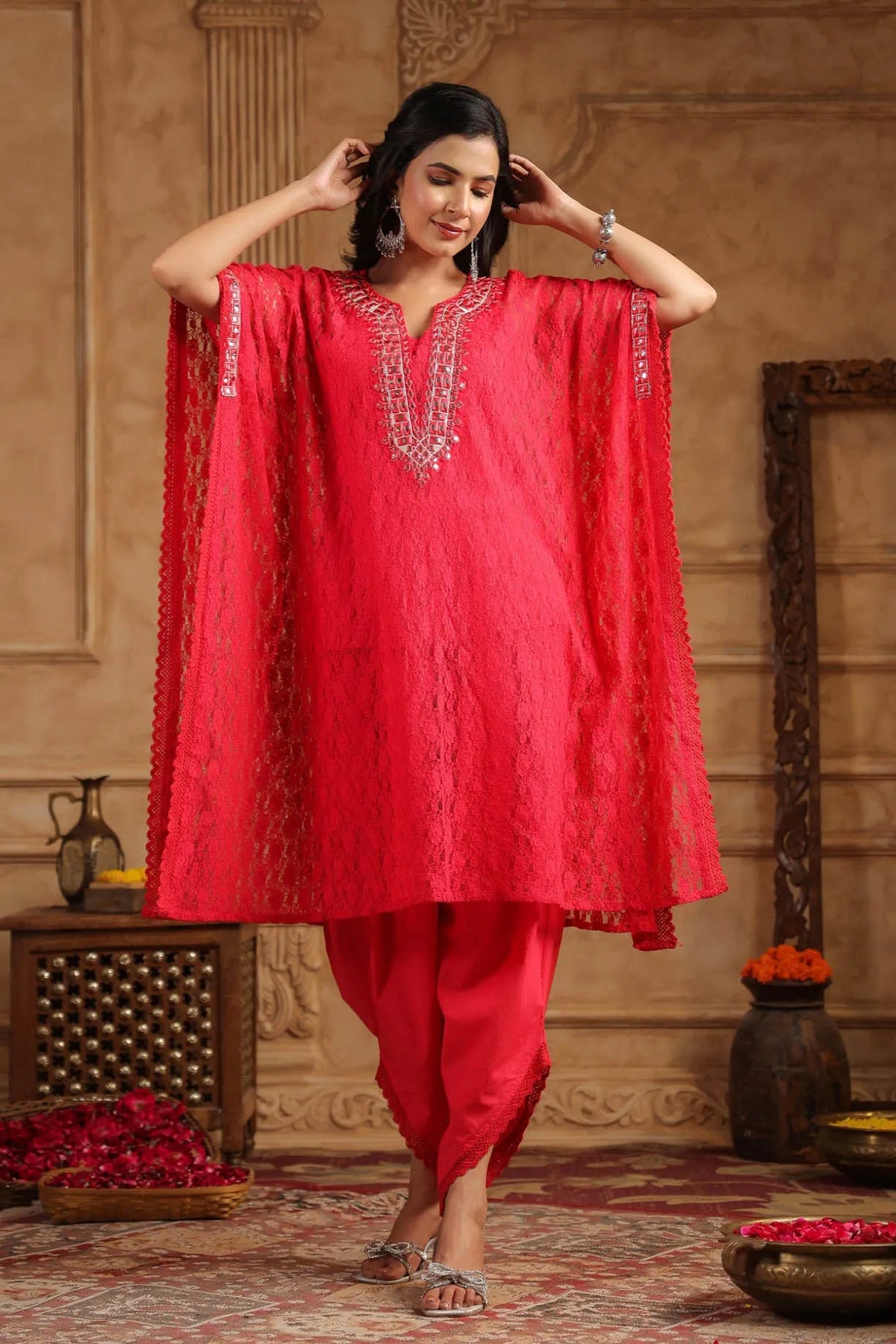 Woman wearing a red traditional outfit with intricate designs in an ornate room.