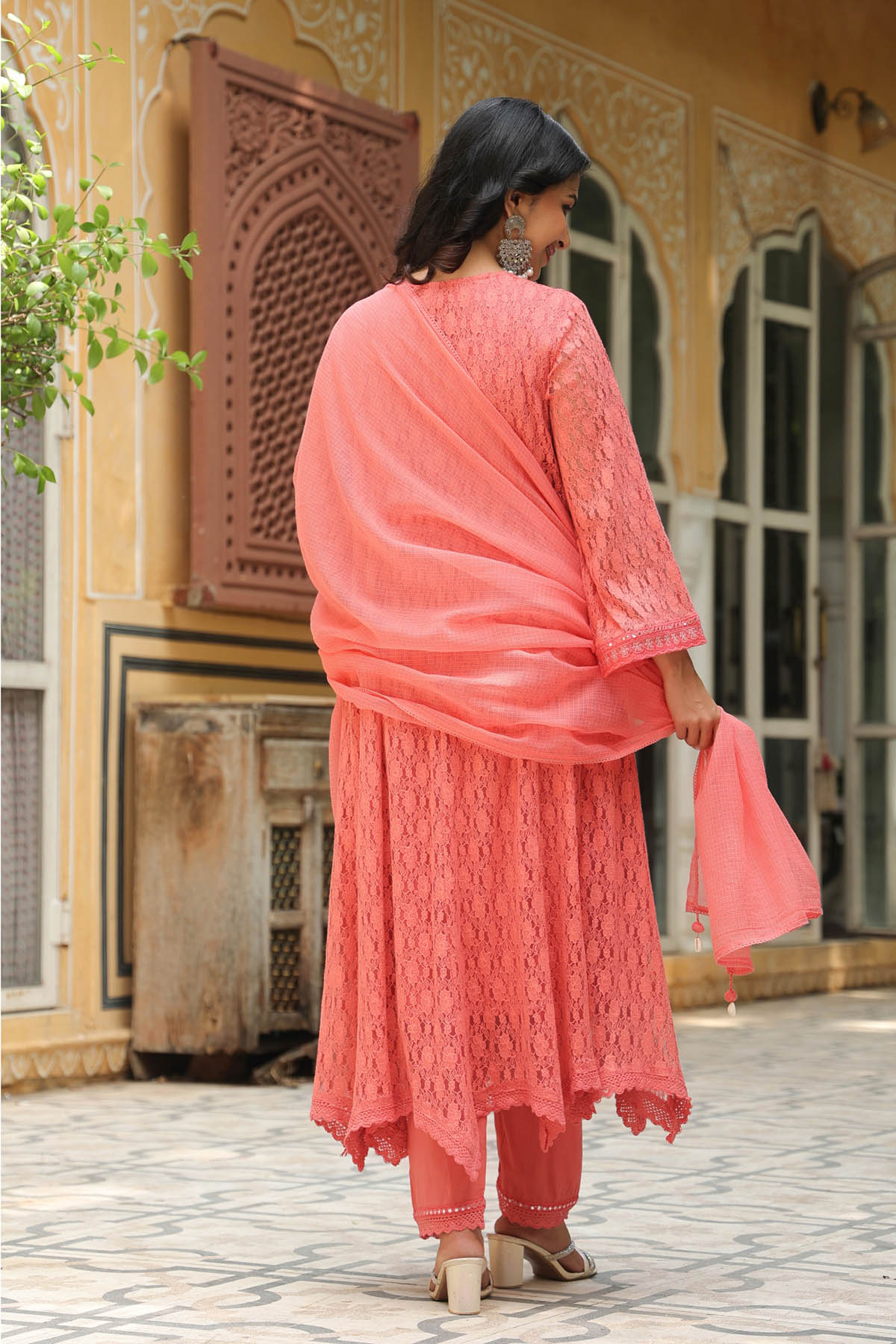 Woman in a coral traditional outfit standing in front of a decorative building.