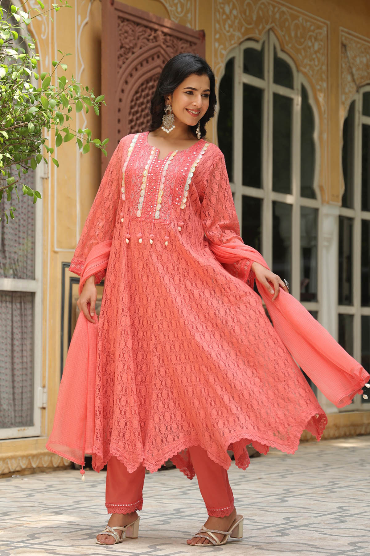 Woman wearing a pink traditional outfit with intricate designs in an outdoor setting.