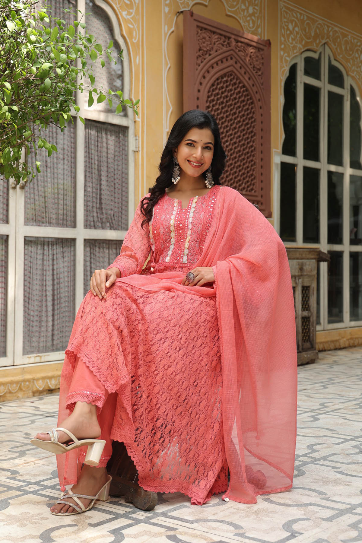Woman in a pink traditional outfit sitting outdoors with decorative architecture in the background
