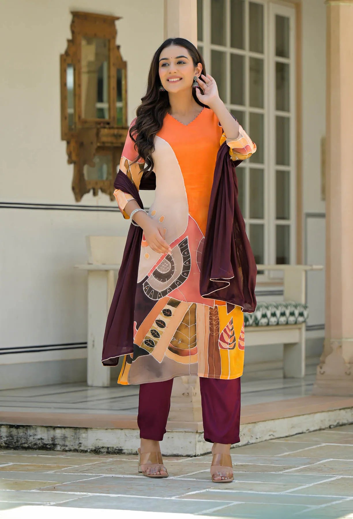 Woman in an orange and purple outfit standing in a decorative indoor setting.