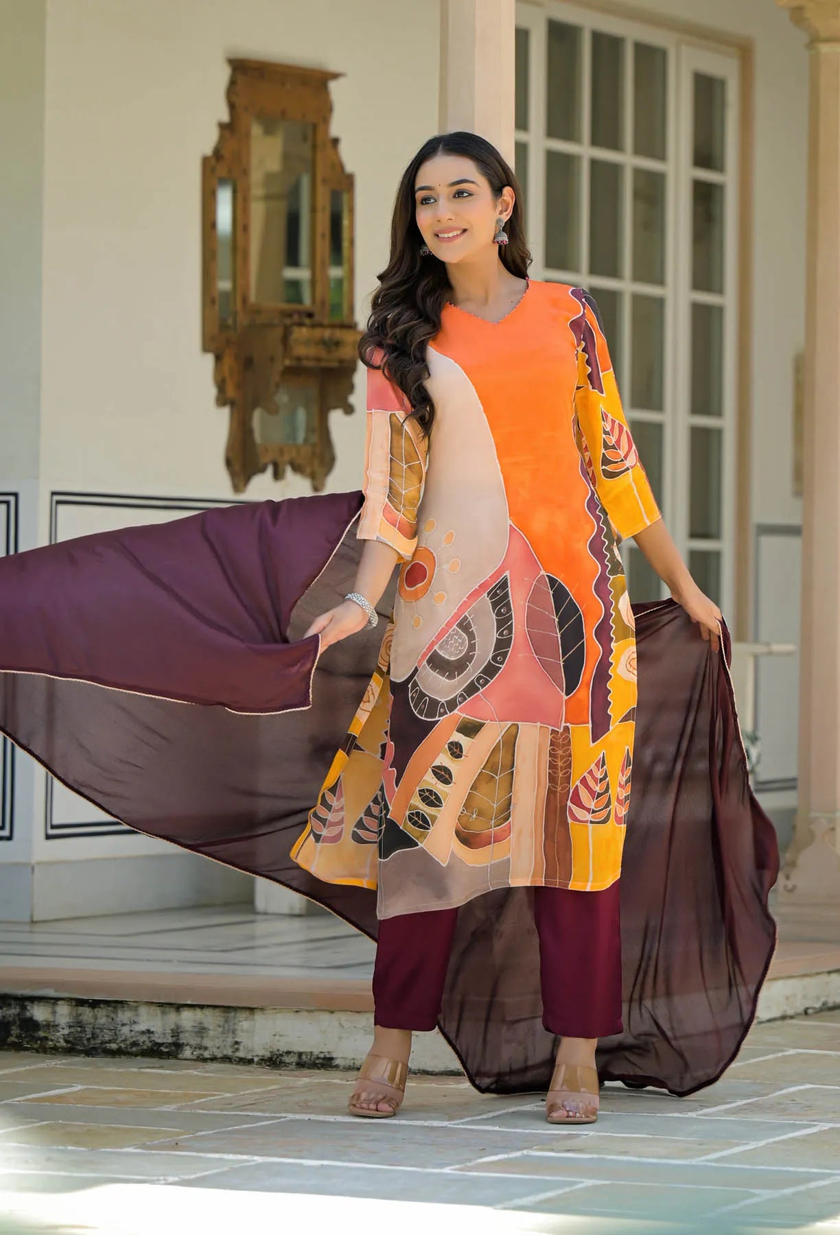 Woman in a colorful traditional outfit with a flowing scarf, standing in a well-lit room.