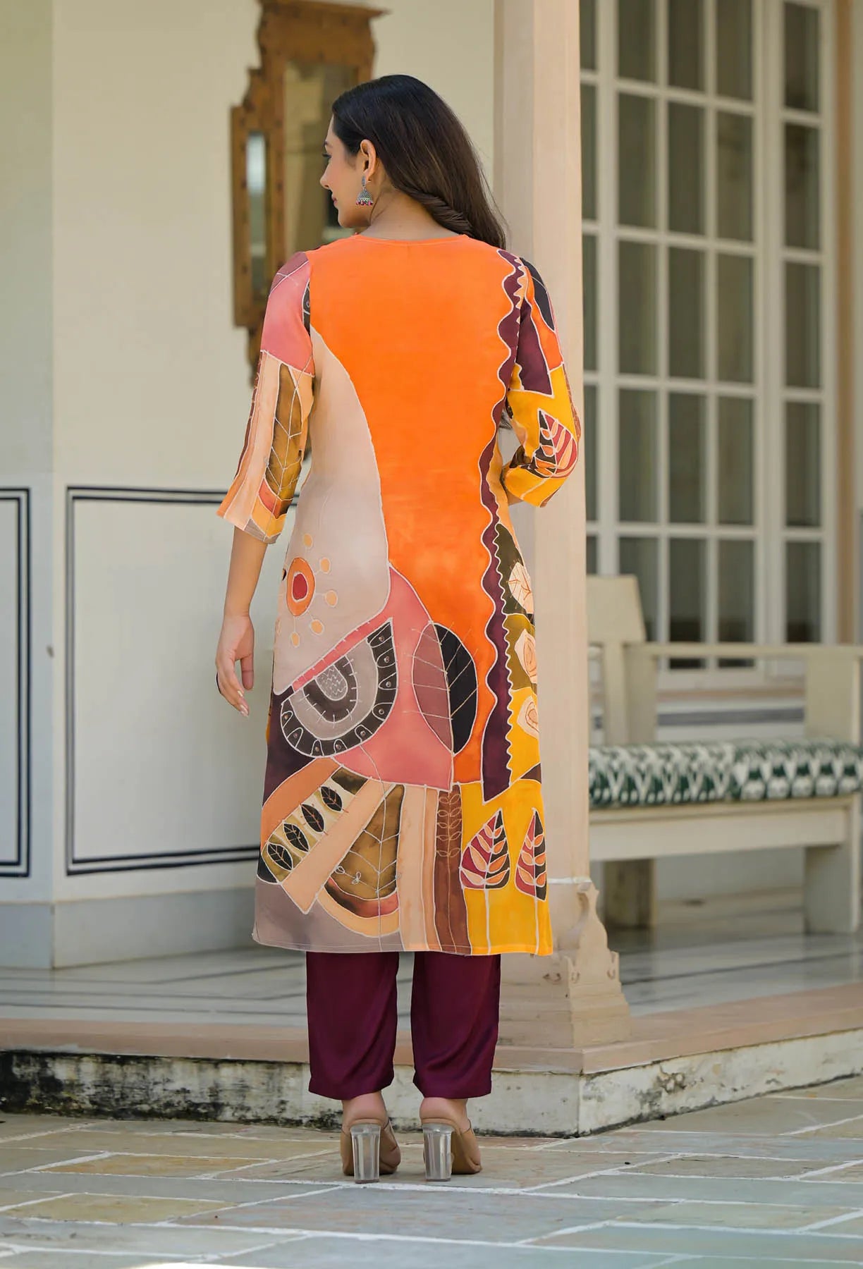 Woman wearing a colorful traditional outfit with a patterned dress and maroon pants, standing in an outdoor setting.