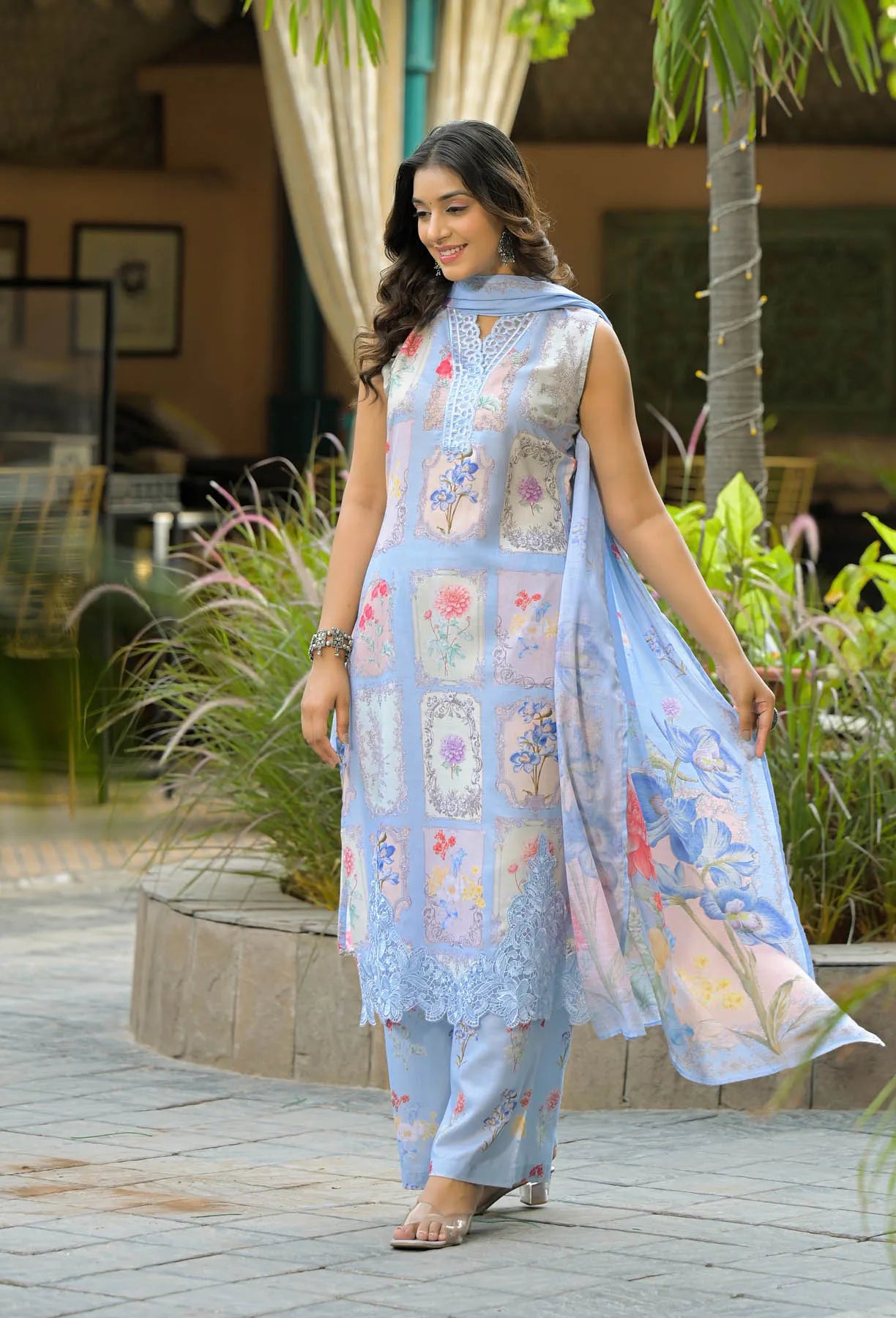 Woman wearing a light blue embroidered outfit with a floral pattern in an outdoor setting.