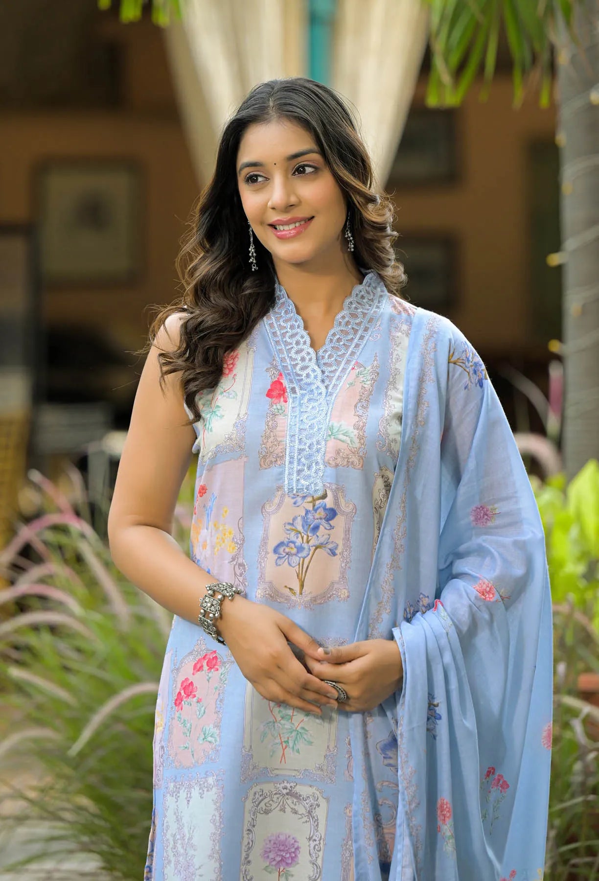 Woman wearing a light blue floral dress standing outdoors with greenery in the background