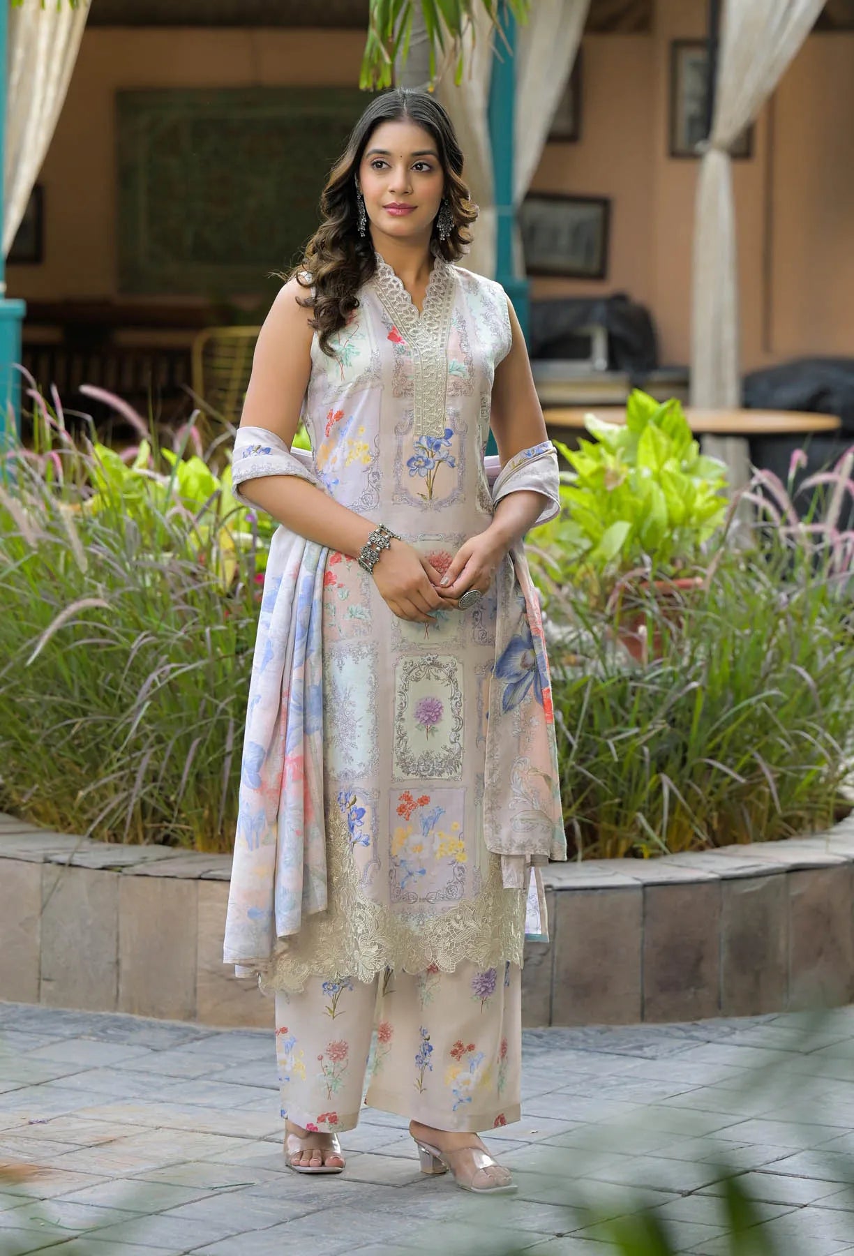 Woman in a floral dress standing outdoors with plants and furniture in the background
