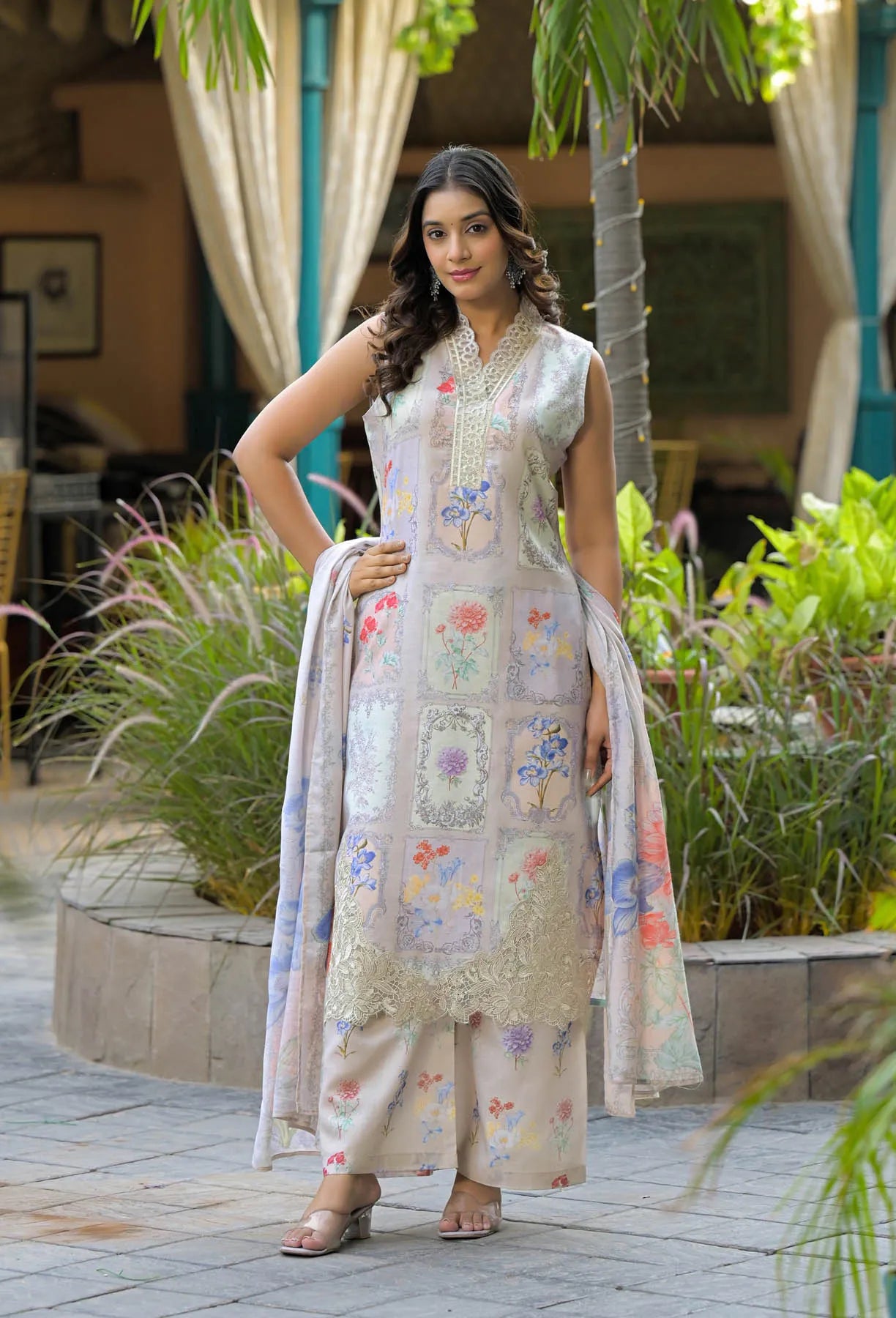 Woman in a floral dress standing outdoors with plants and a building in the background