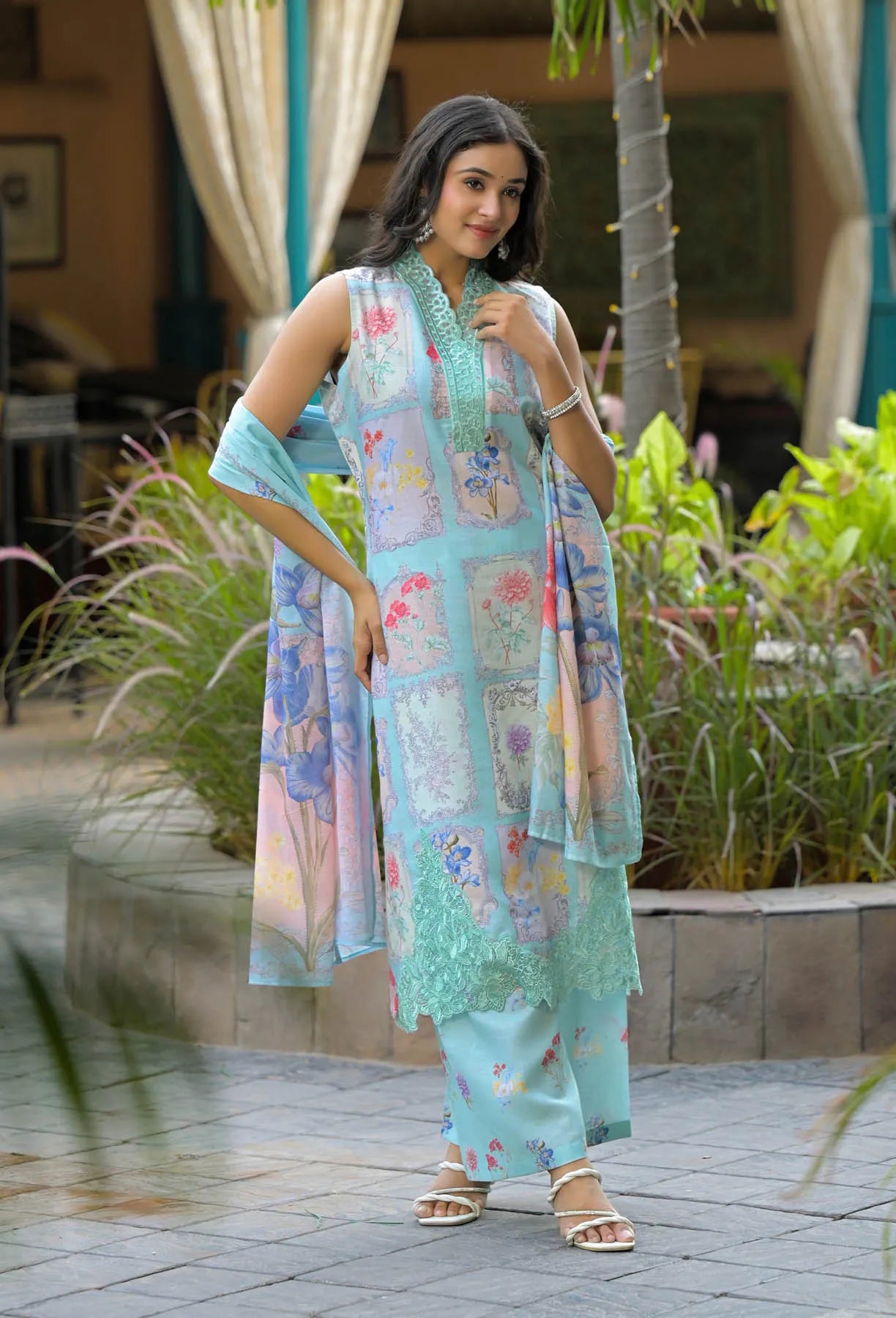 Woman in a floral dress standing outdoors with plants and a building in the background