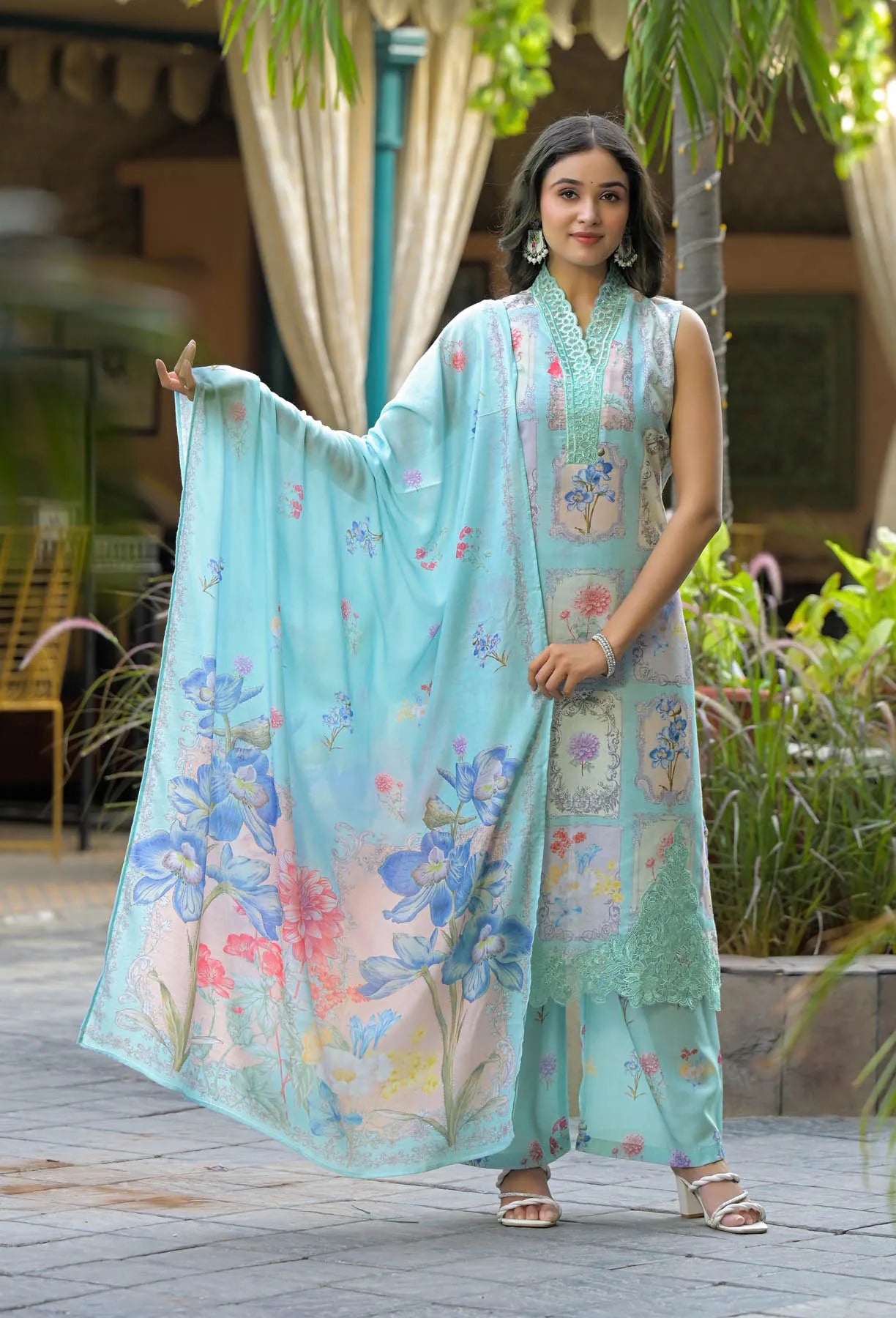 Woman in a light blue floral dress holding a matching dupatta outdoors.