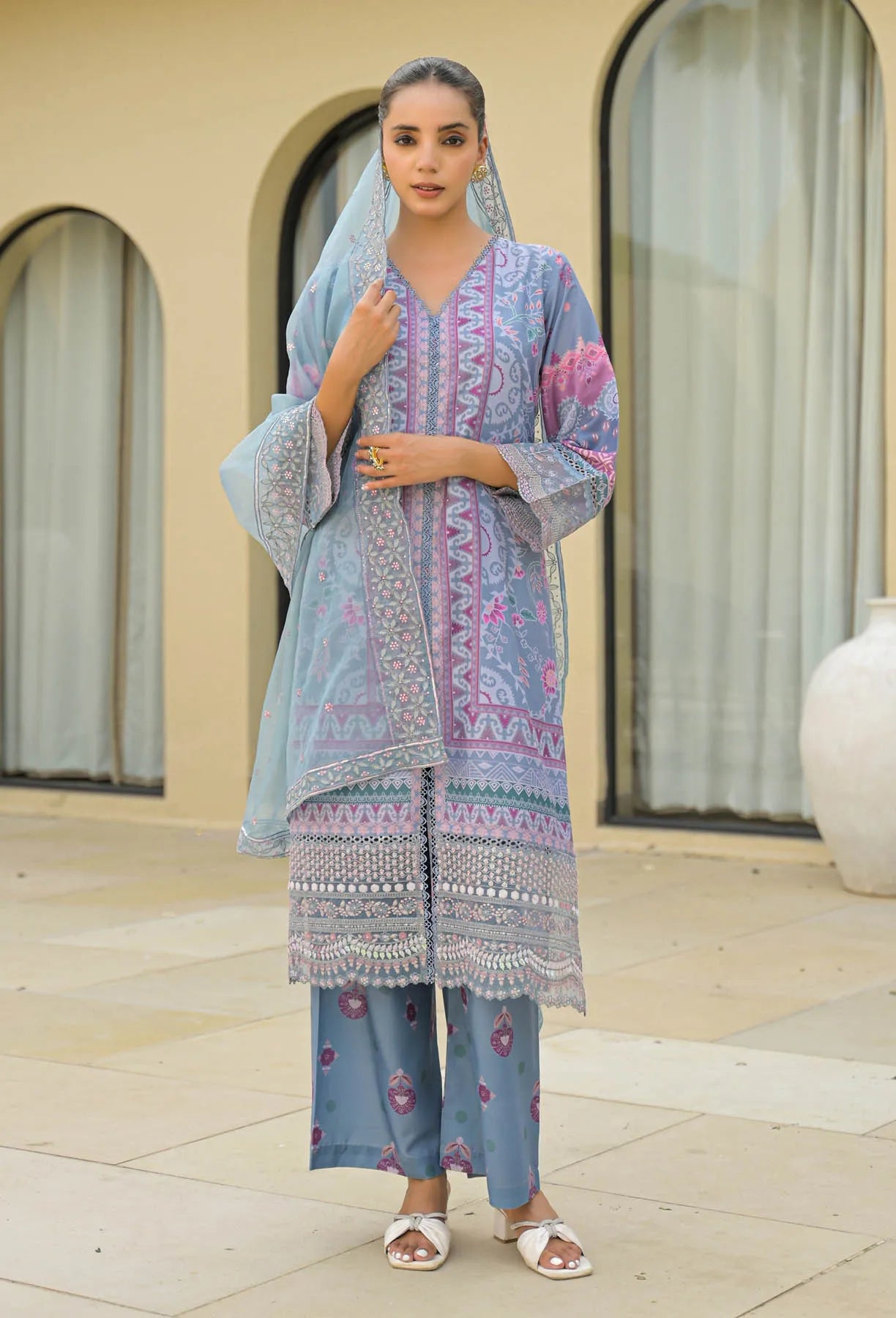 Woman wearing a traditional outfit with a light blue dupatta and pink embroidered top in an outdoor setting.