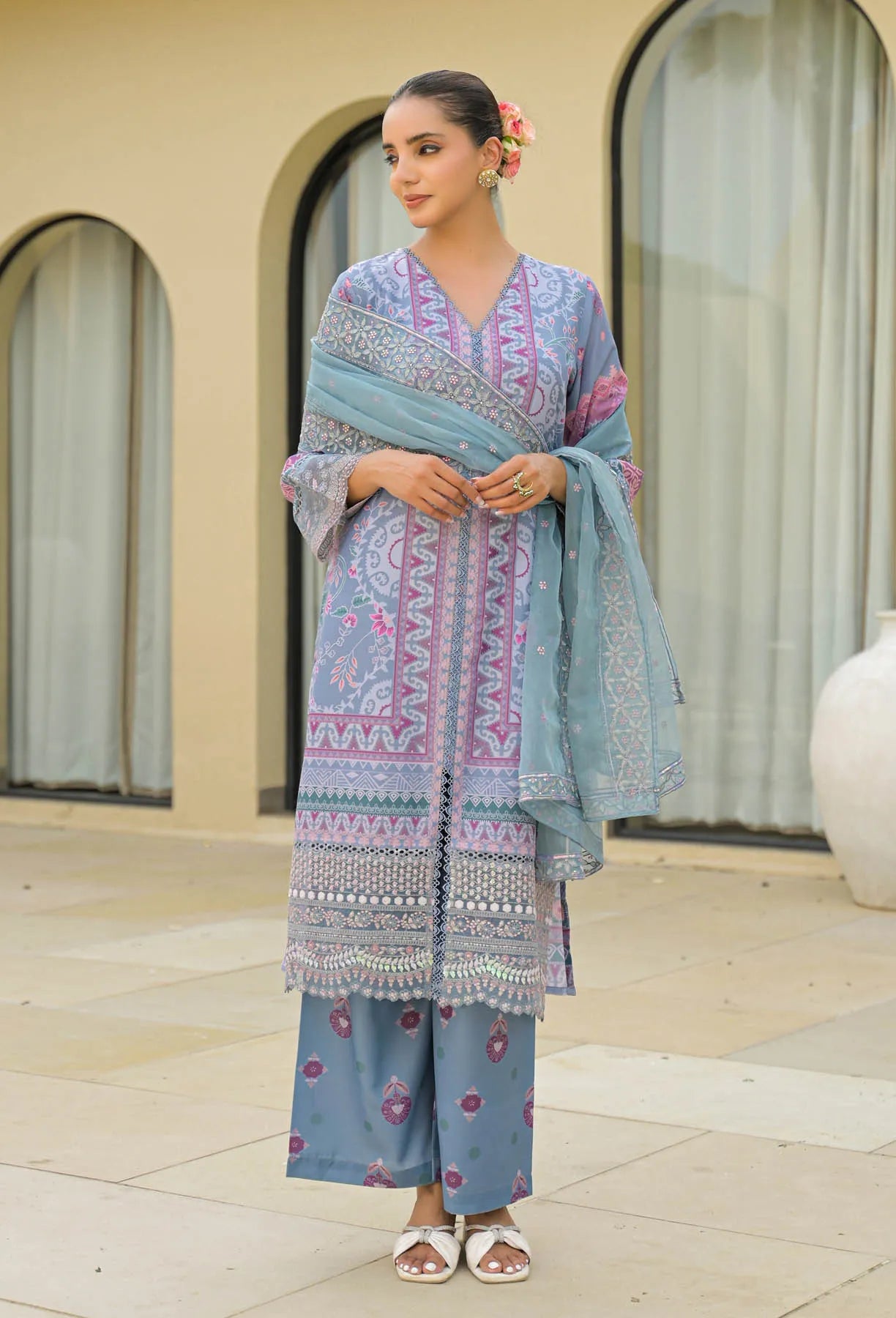 Woman wearing a traditional outfit with a blue and pink patterned dupatta, standing outdoors.