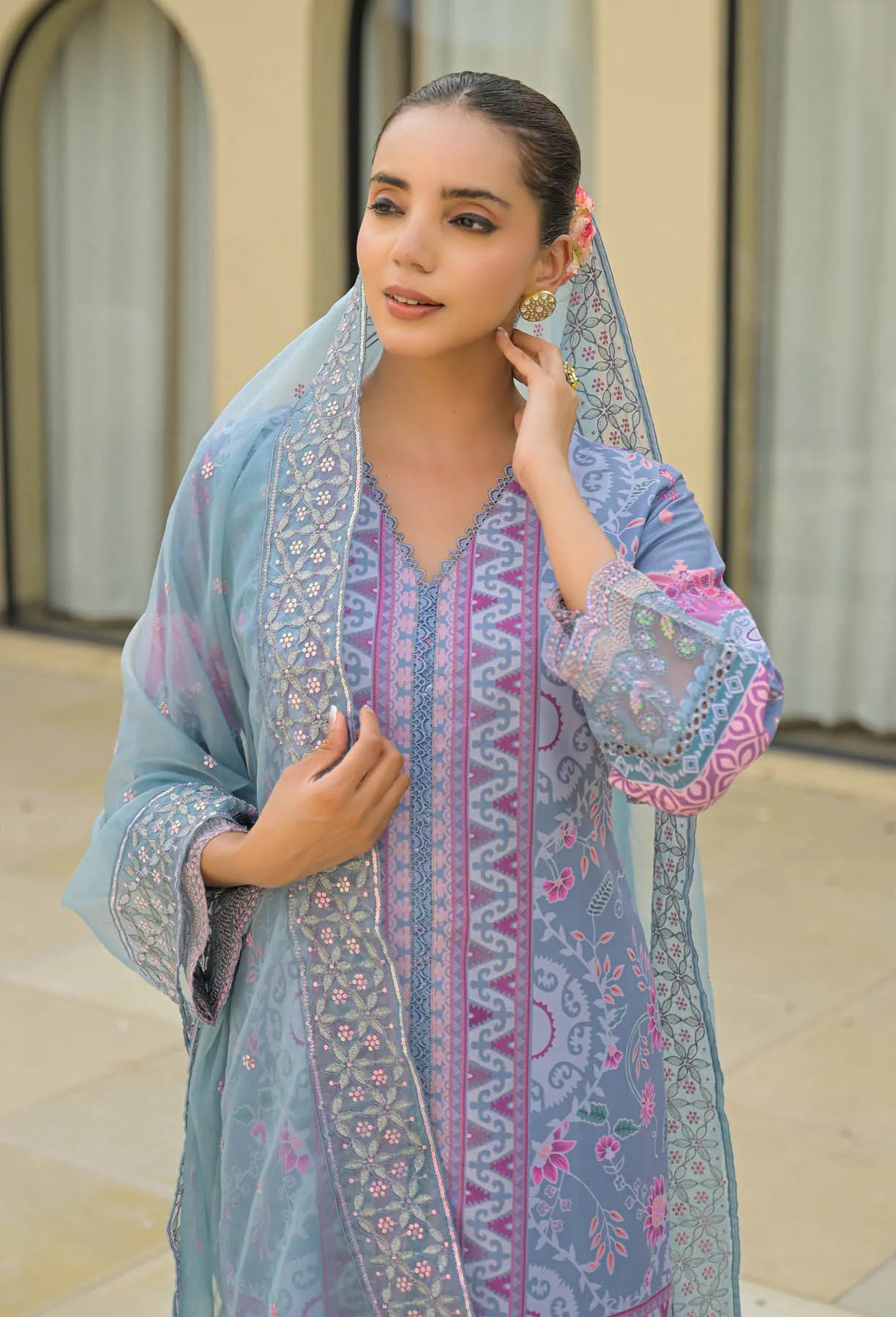 Woman wearing a light blue and pink embroidered traditional outfit with a matching dupatta.