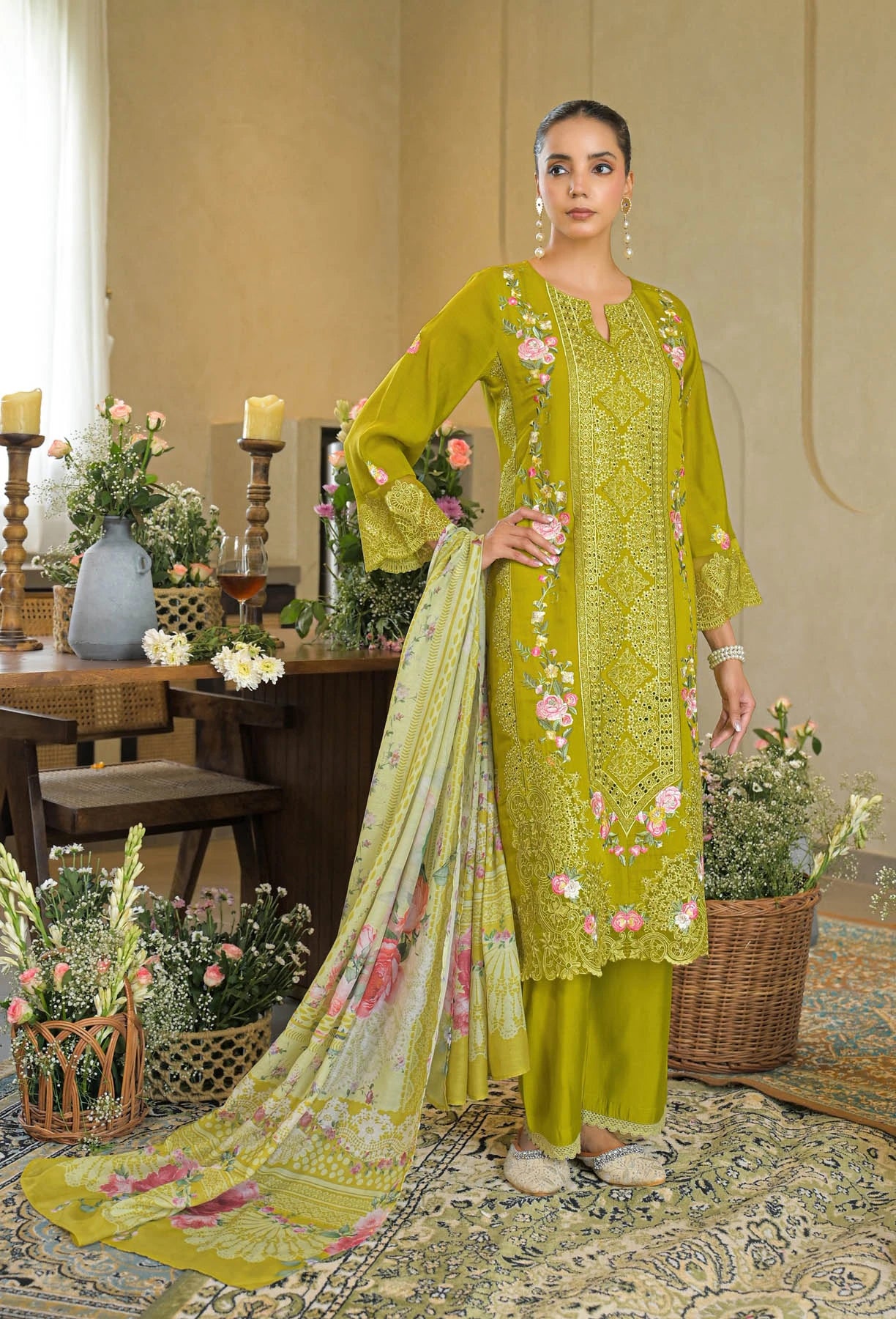 Woman in a green embroidered outfit standing in a decorated room with flowers and candles.
