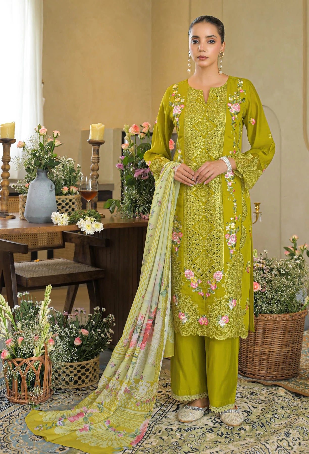 Woman in a green embroidered outfit standing in a decorated room with flowers and candles.