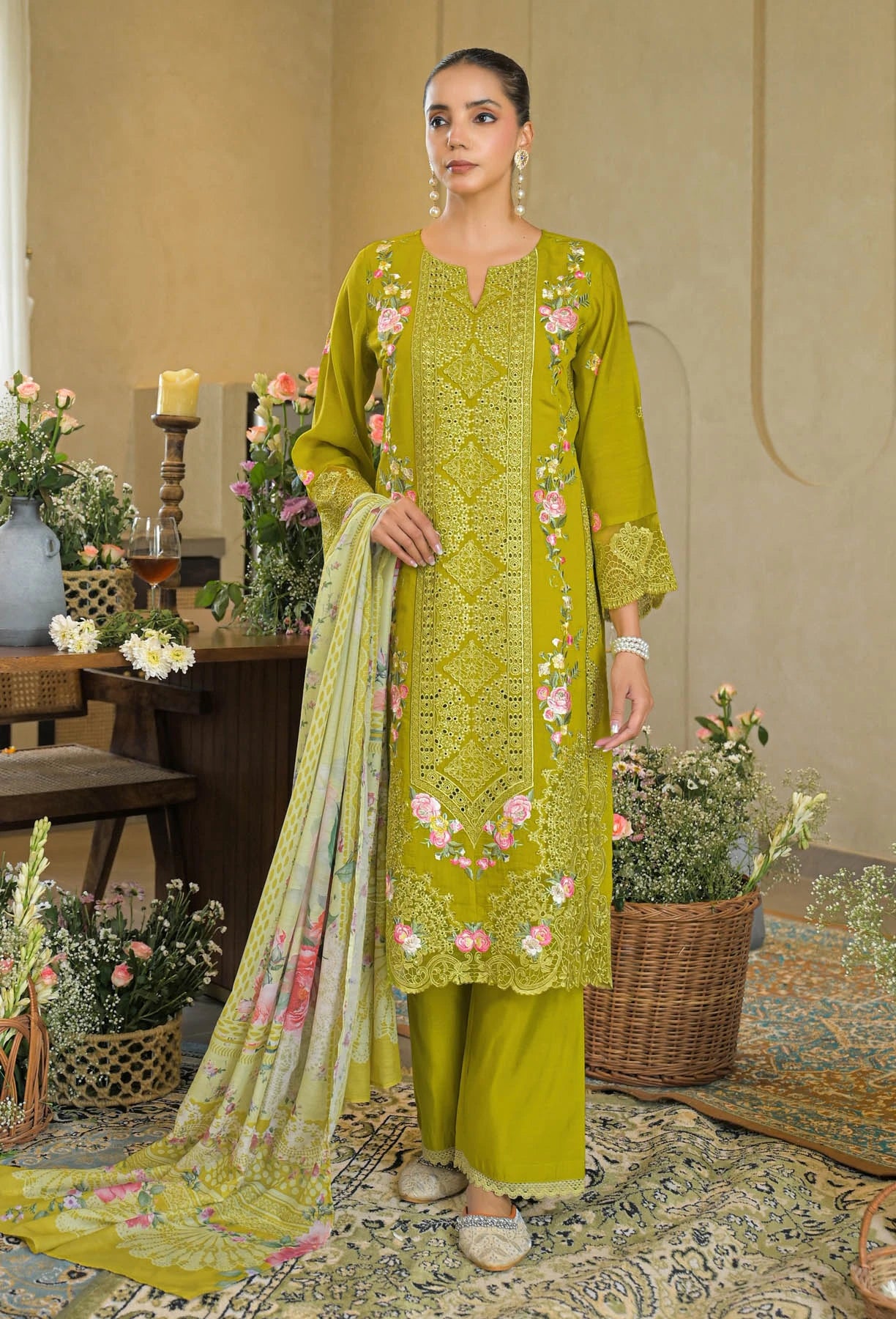 Woman wearing a green embroidered outfit with a matching dupatta in a decorated room.
