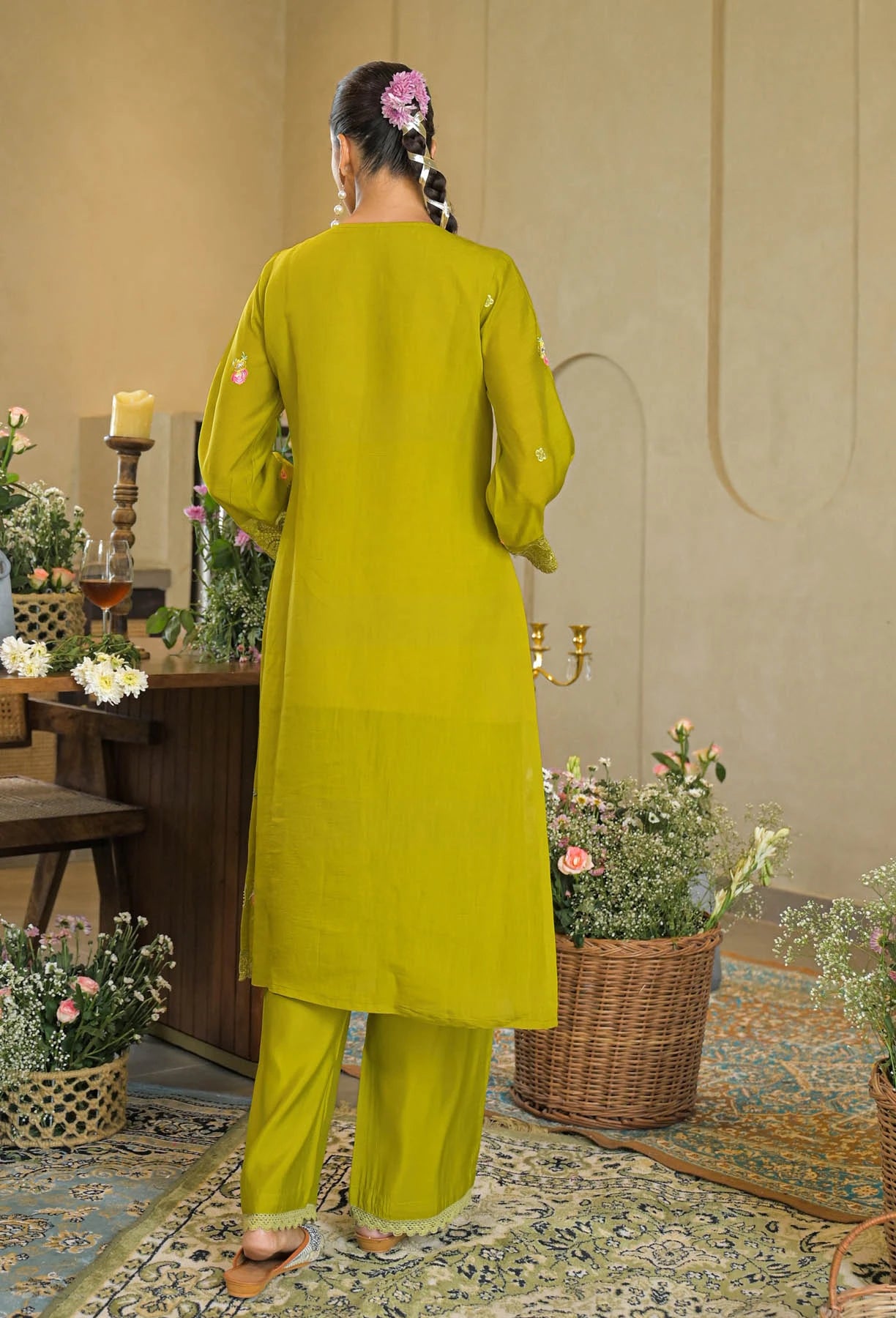 Woman in a green outfit standing in a room with floral decorations and a candle.