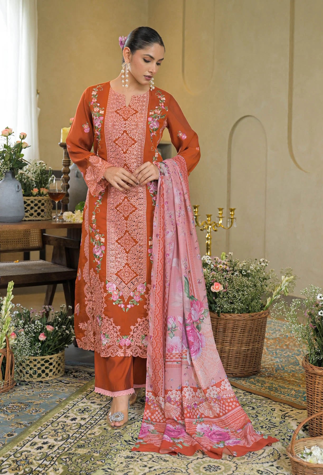 Woman in traditional embroidered outfit with pink dupatta in a decorated room.