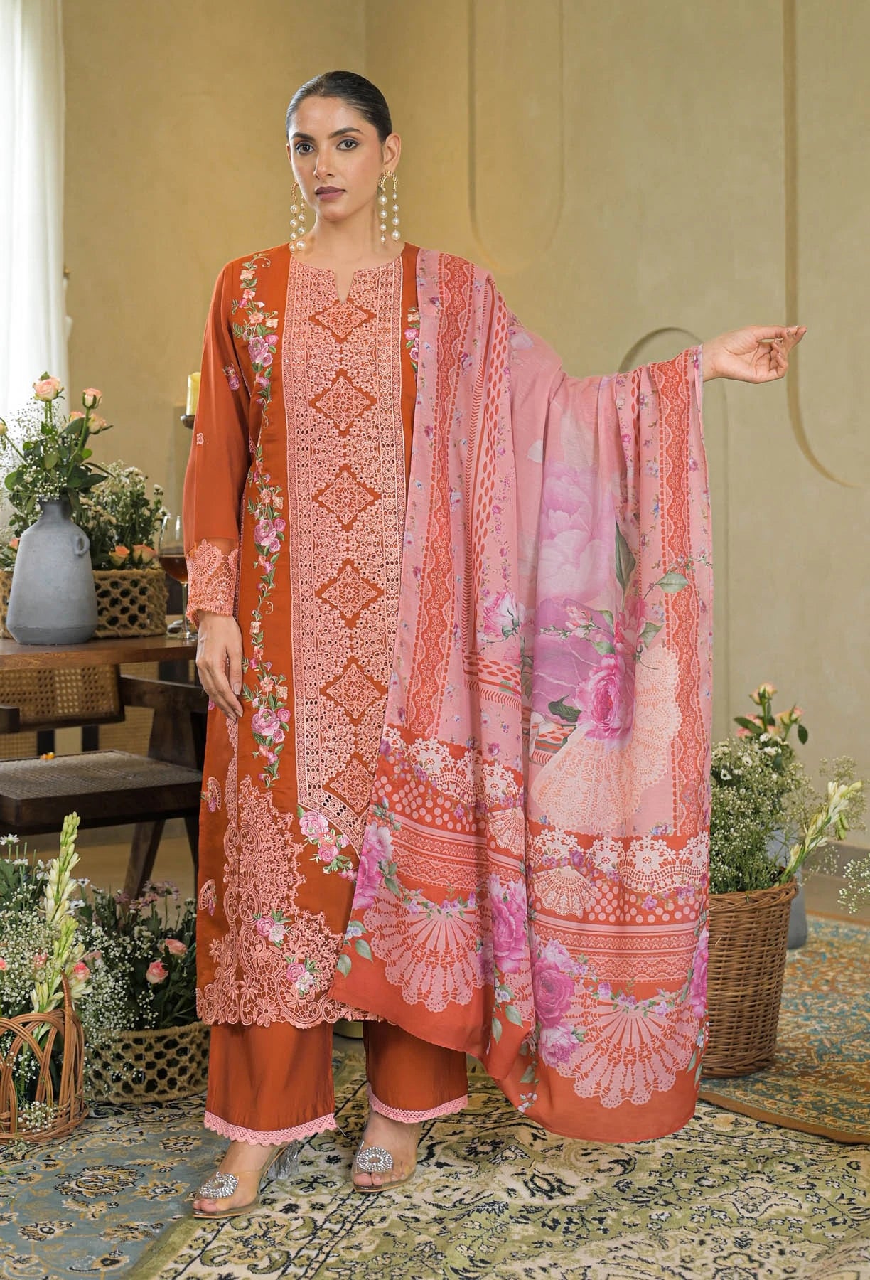 Woman wearing a traditional outfit with a pink and orange dupatta in a decorated room.