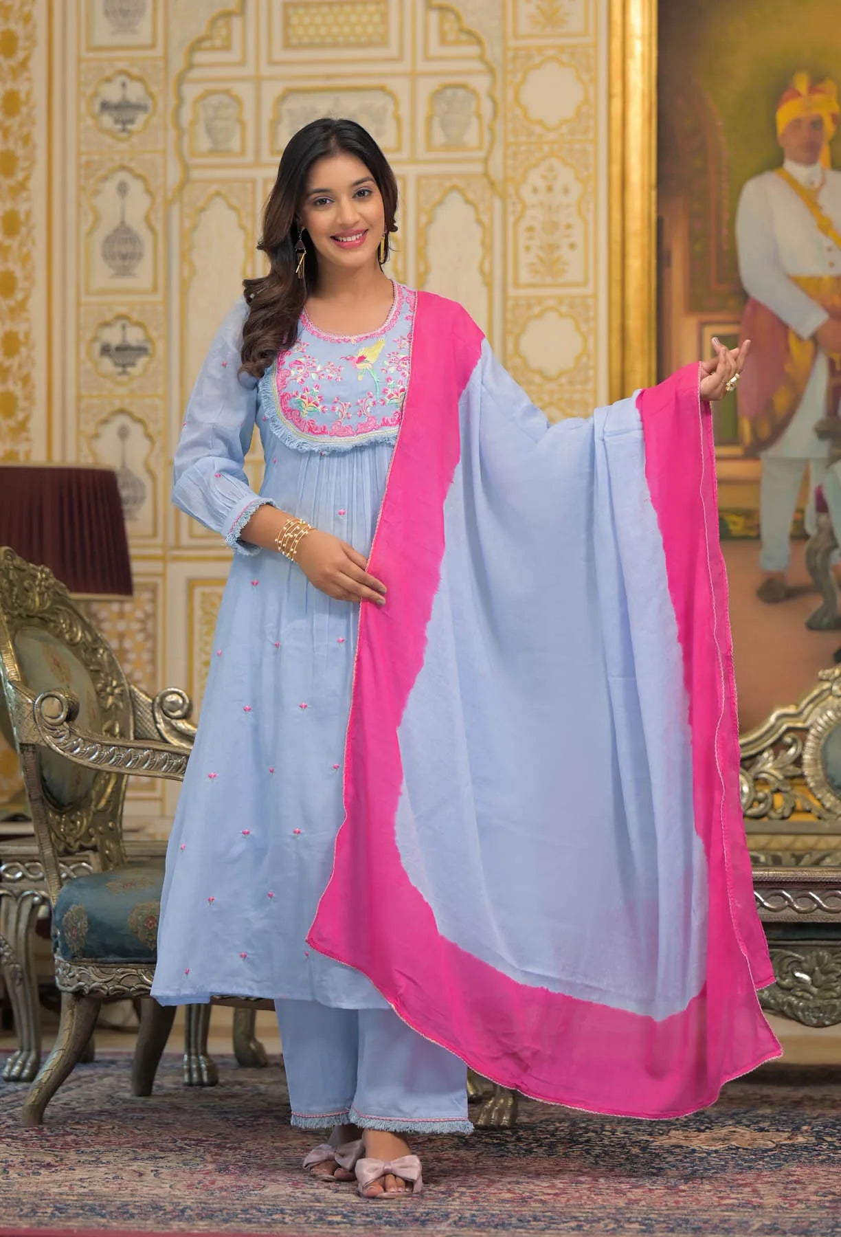 Woman in traditional outfit with light blue dress and pink dupatta in ornate room