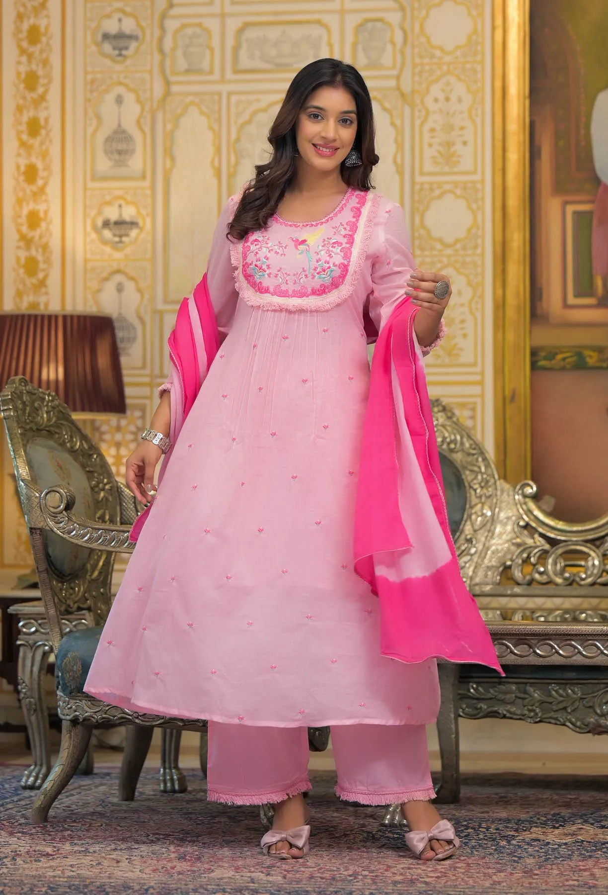 Woman in a pink traditional outfit with a matching dupatta in a decorated room.