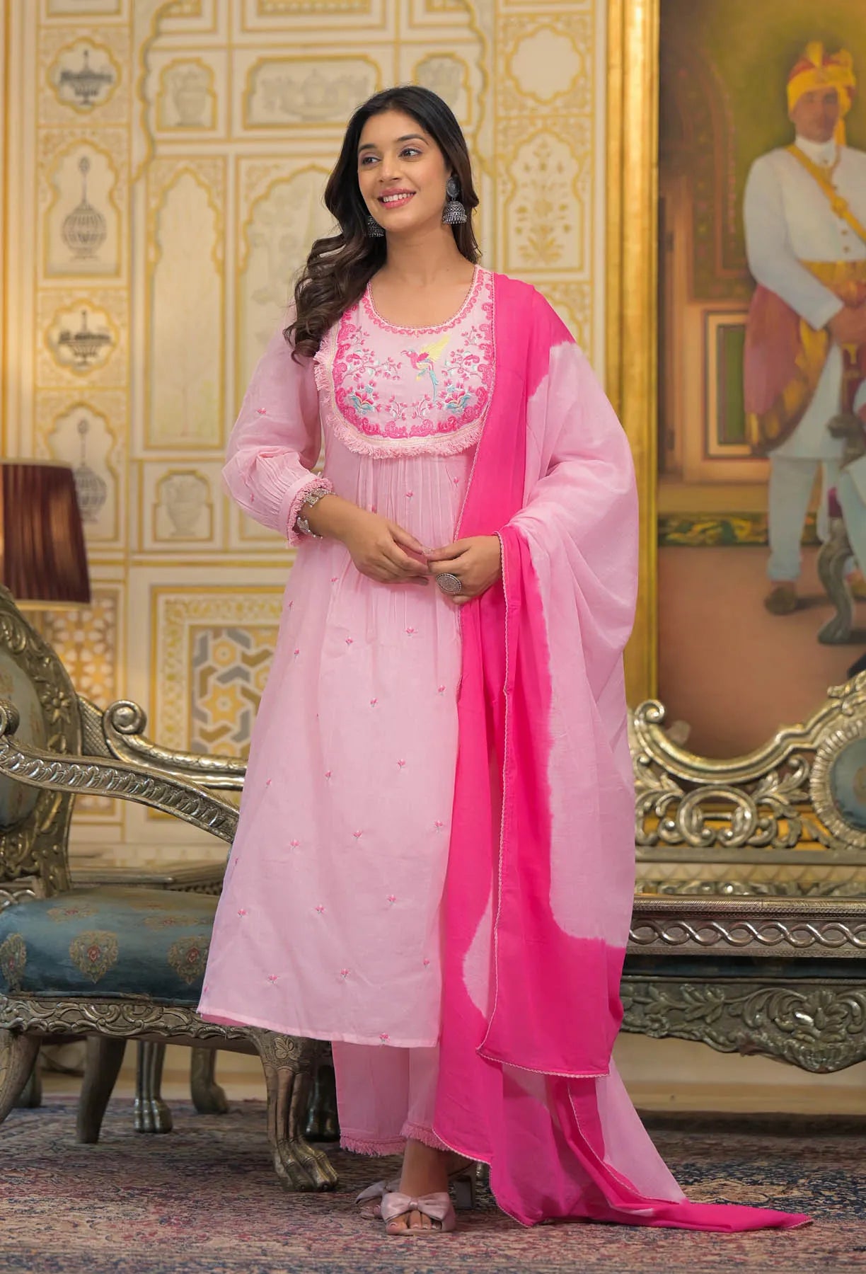 Woman in a pink traditional outfit standing in an ornate room.
