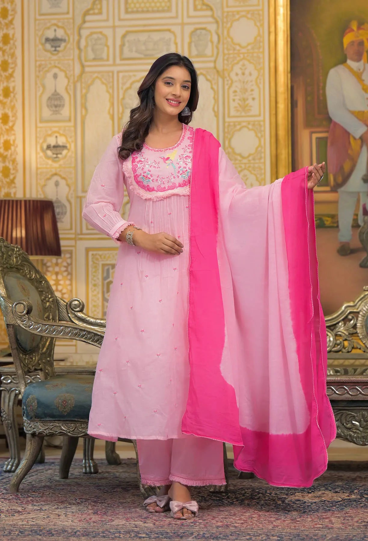 Woman in a pink traditional outfit with a matching dupatta in a decorated room.
