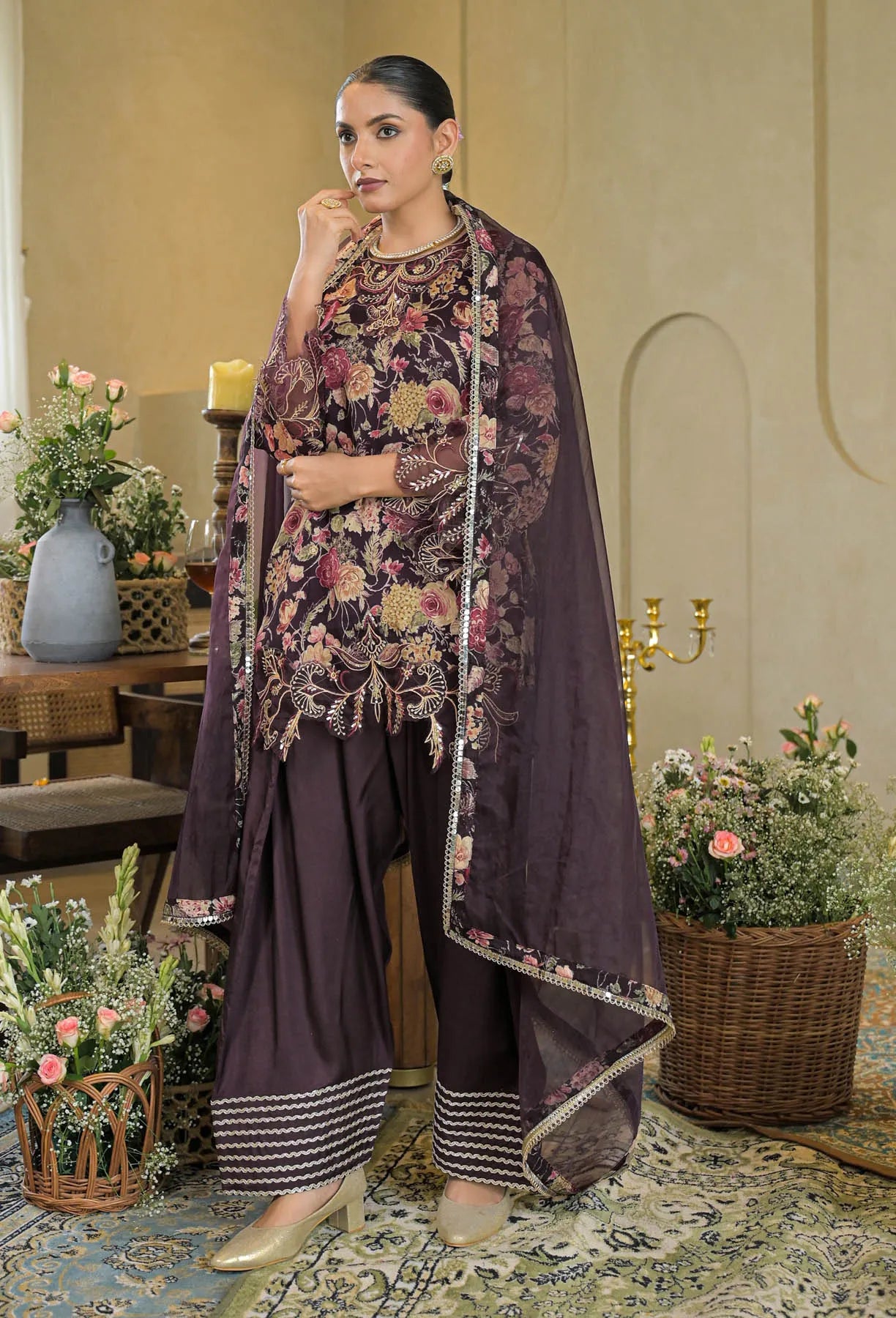 Woman in a traditional outfit with floral patterns in a decorated room.