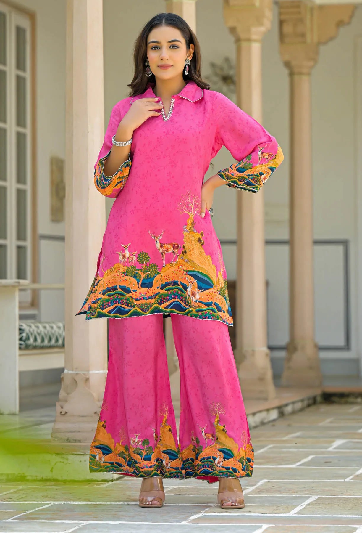 Woman wearing a bright pink traditional outfit with colorful embroidery in an outdoor setting.