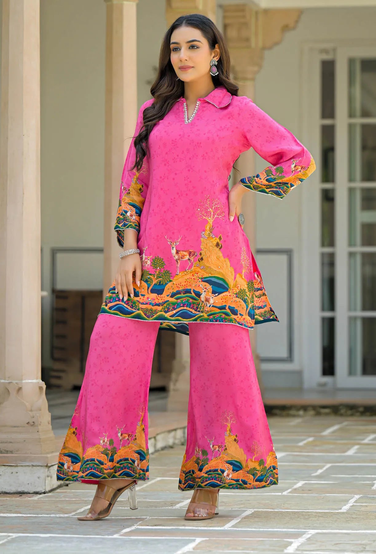Woman wearing a bright pink traditional outfit with colorful patterns in an outdoor setting.
