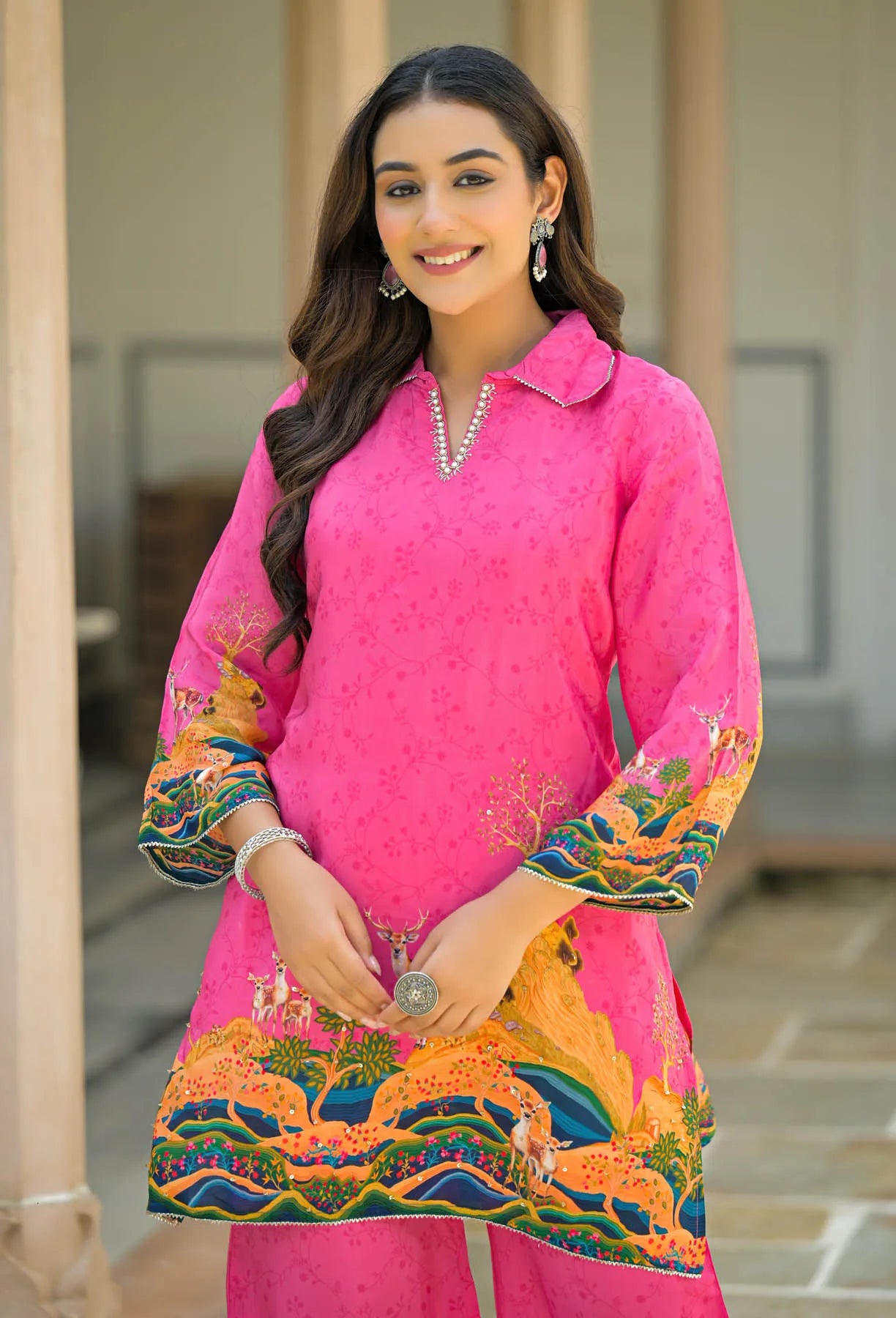 Woman wearing a bright pink traditional outfit with colorful embroidery, standing outdoors.