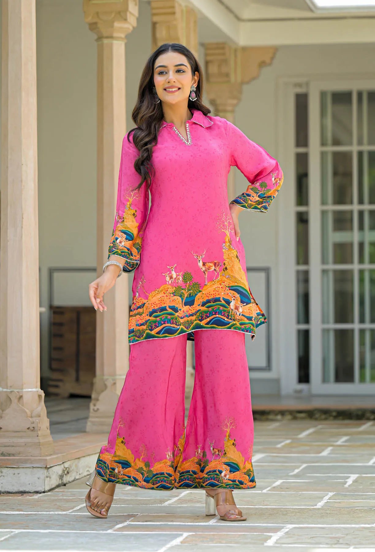 Woman wearing a bright pink traditional outfit with colorful embroidery in an outdoor setting.