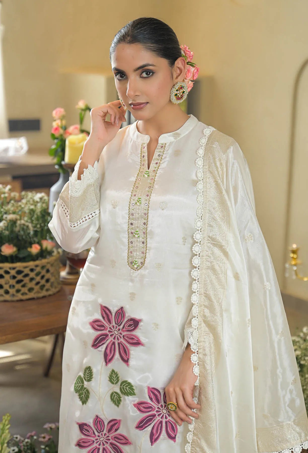 Woman wearing a white embroidered traditional outfit with pink flowers indoors.