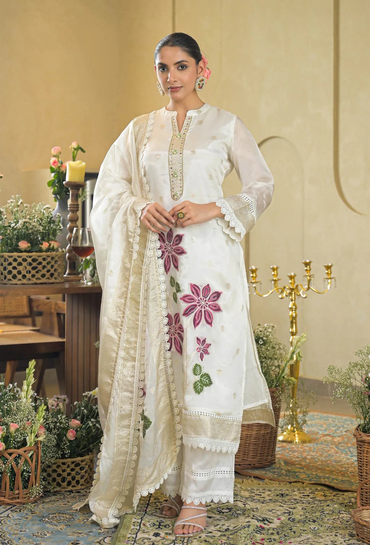 Woman wearing a white embroidered traditional outfit with pink flowers indoors.