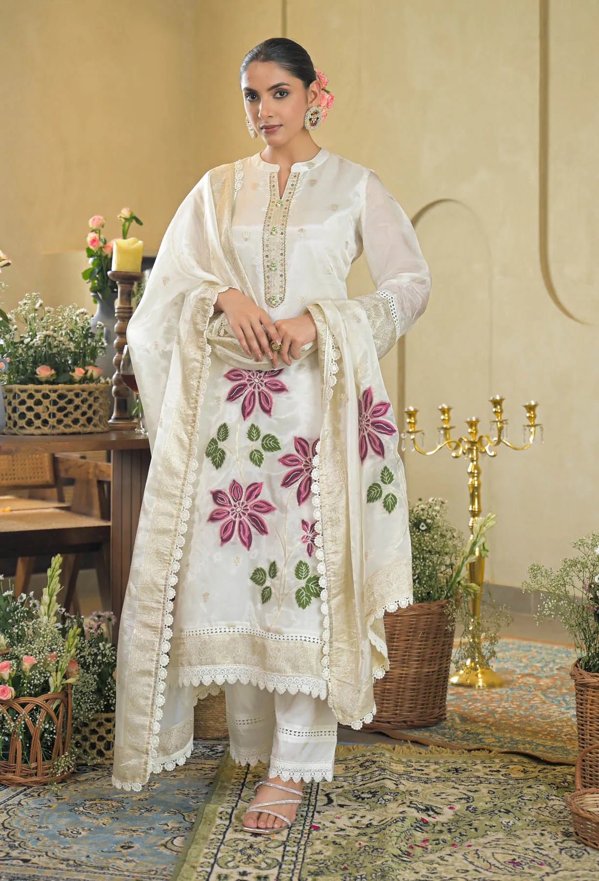 Woman wearing a white embroidered outfit in an elegant indoor setting with floral decorations.