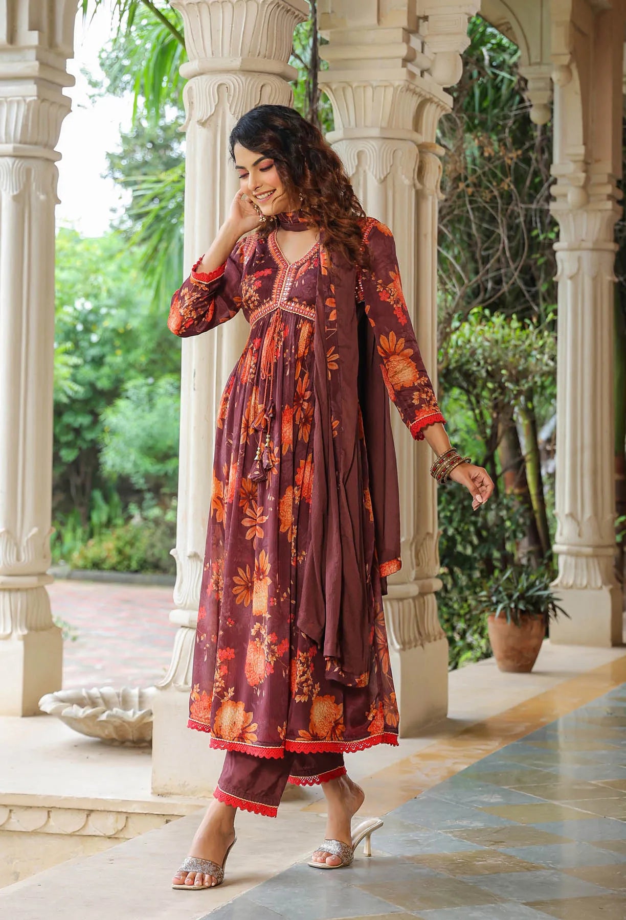 Woman in a floral dress standing in an outdoor setting with columns and greenery.