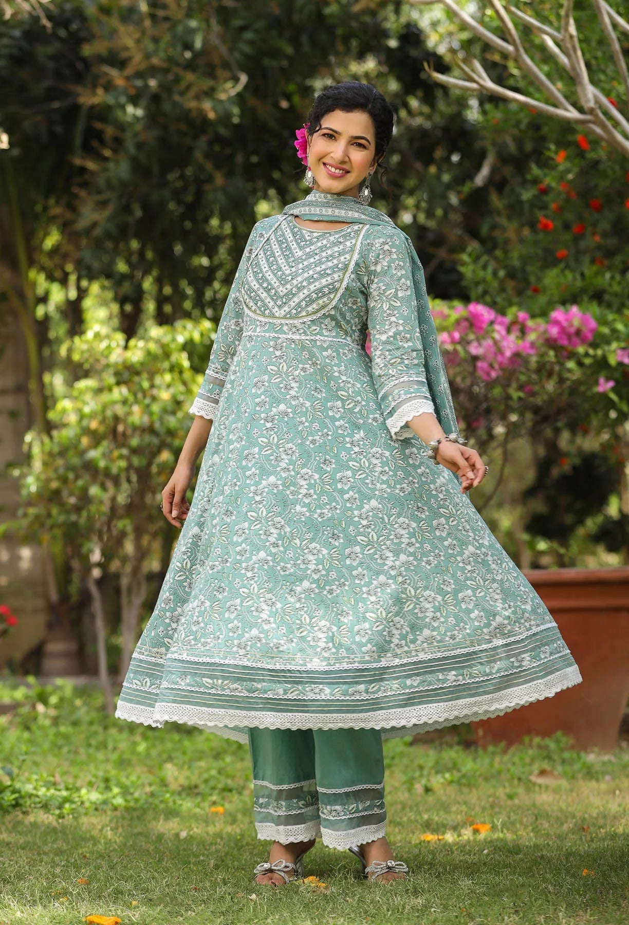 Woman wearing a green traditional outfit with white patterns in an outdoor setting.